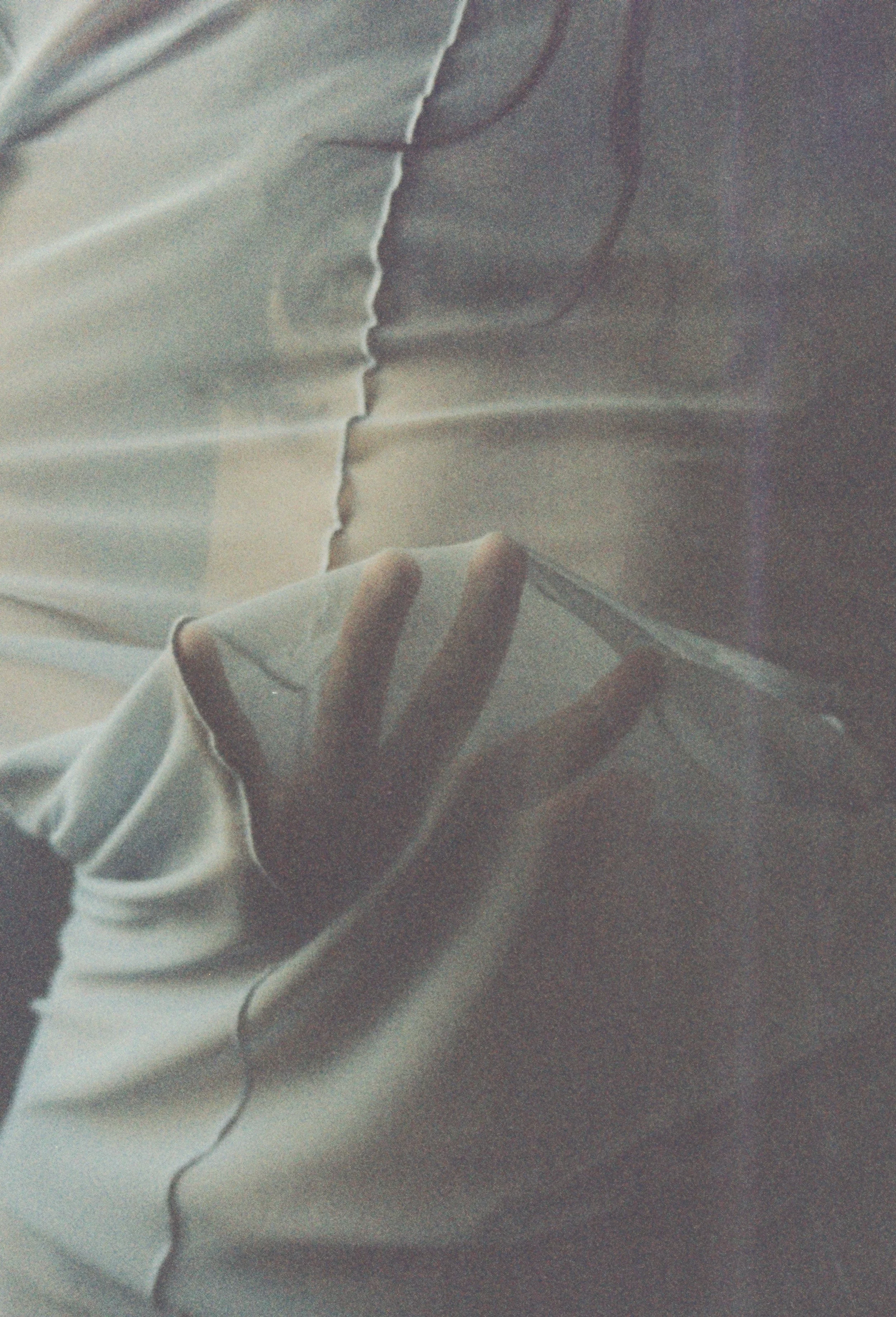 Close-up of white fabric with a hand holding the edge, showing wrinkles and a seam.