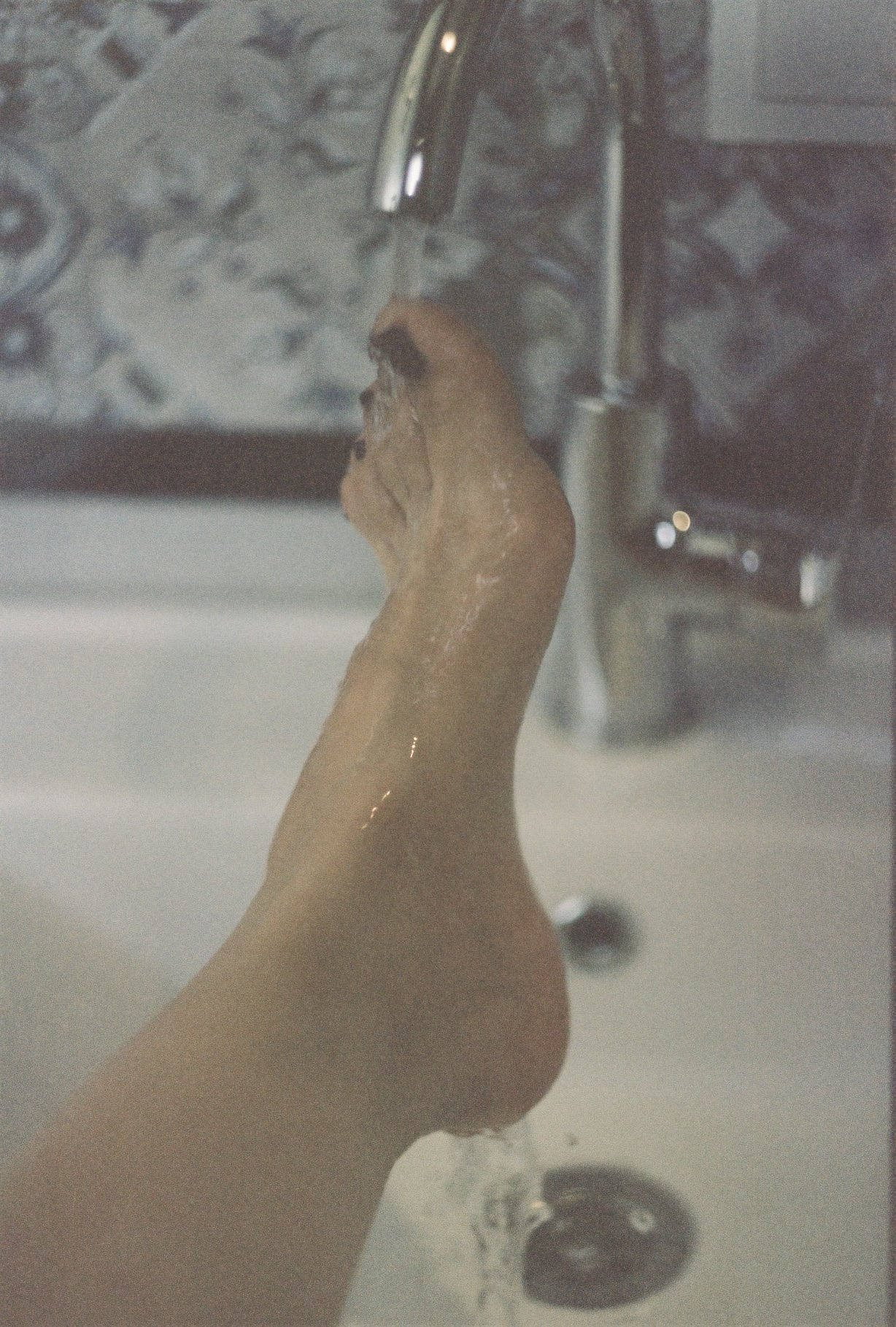 A person's hand under running water from a faucet in a kitchen sink.