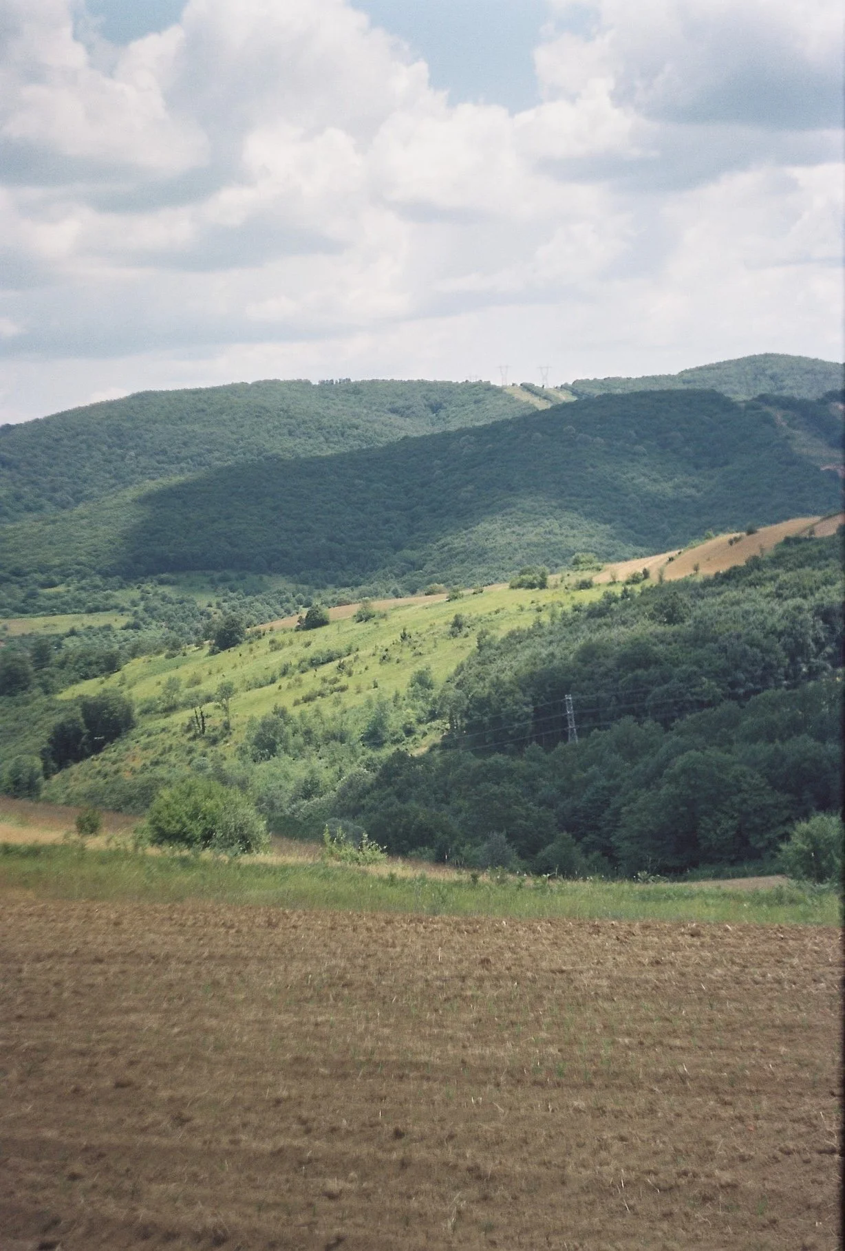 Scenic view of rolling green hills with farmland and power lines under partly cloudy sky.