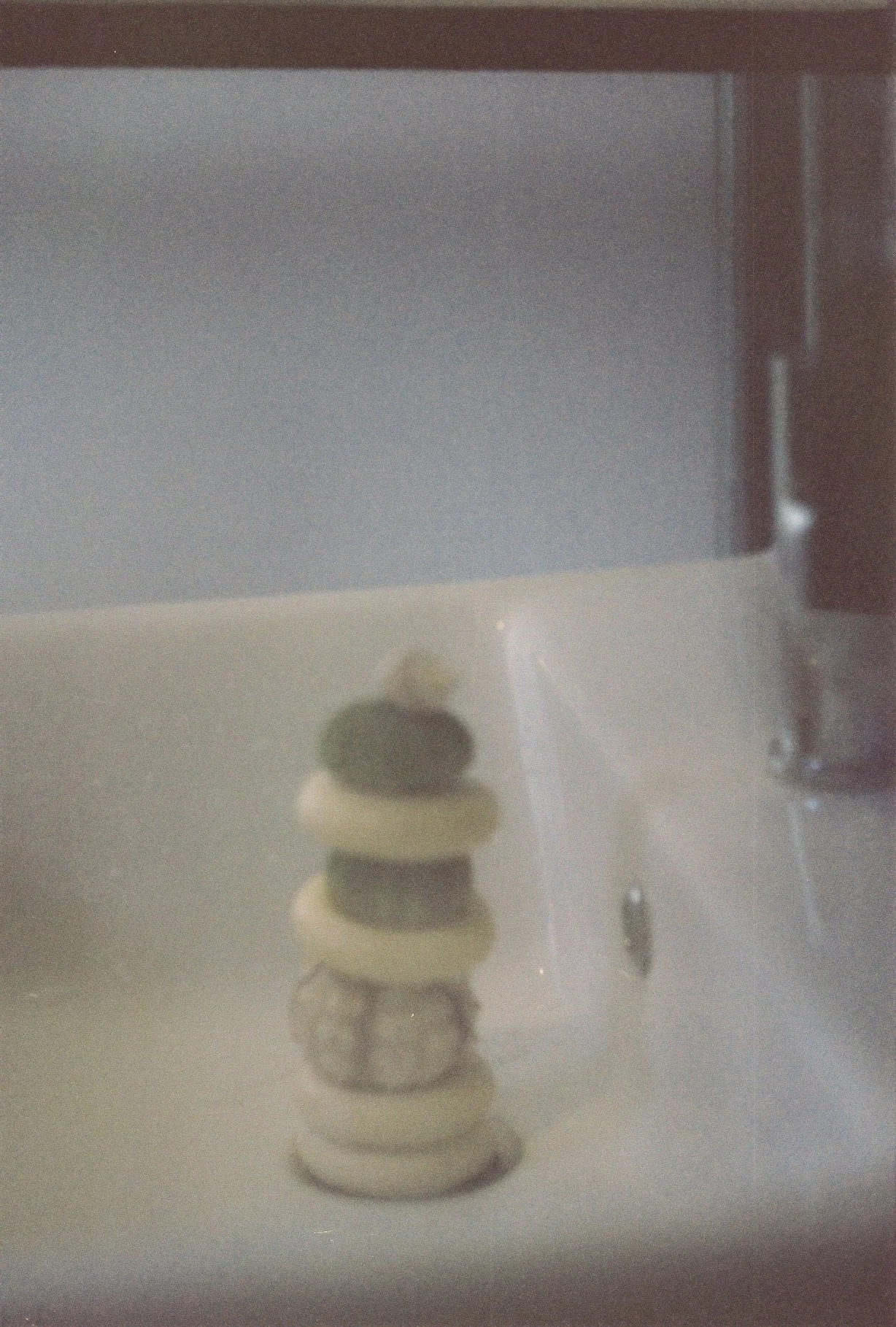 A small sculpture featuring a stack of circular, cream-colored objects with a dark, textured sphere at the top, placed on a reflective surface with a blurred background.