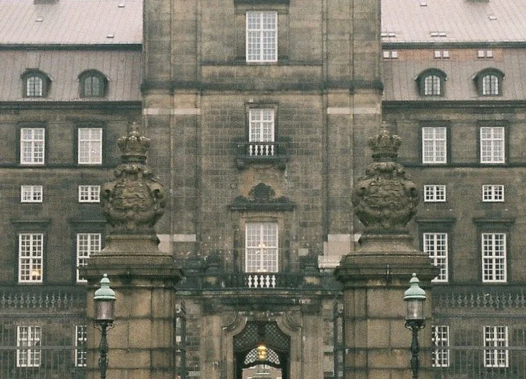 The image shows the entrance of a historic stone building with two large stone lion statues on pedestals on either side of the entrance. There are street lamps in front, and the building features multiple windows with some having small balconies.