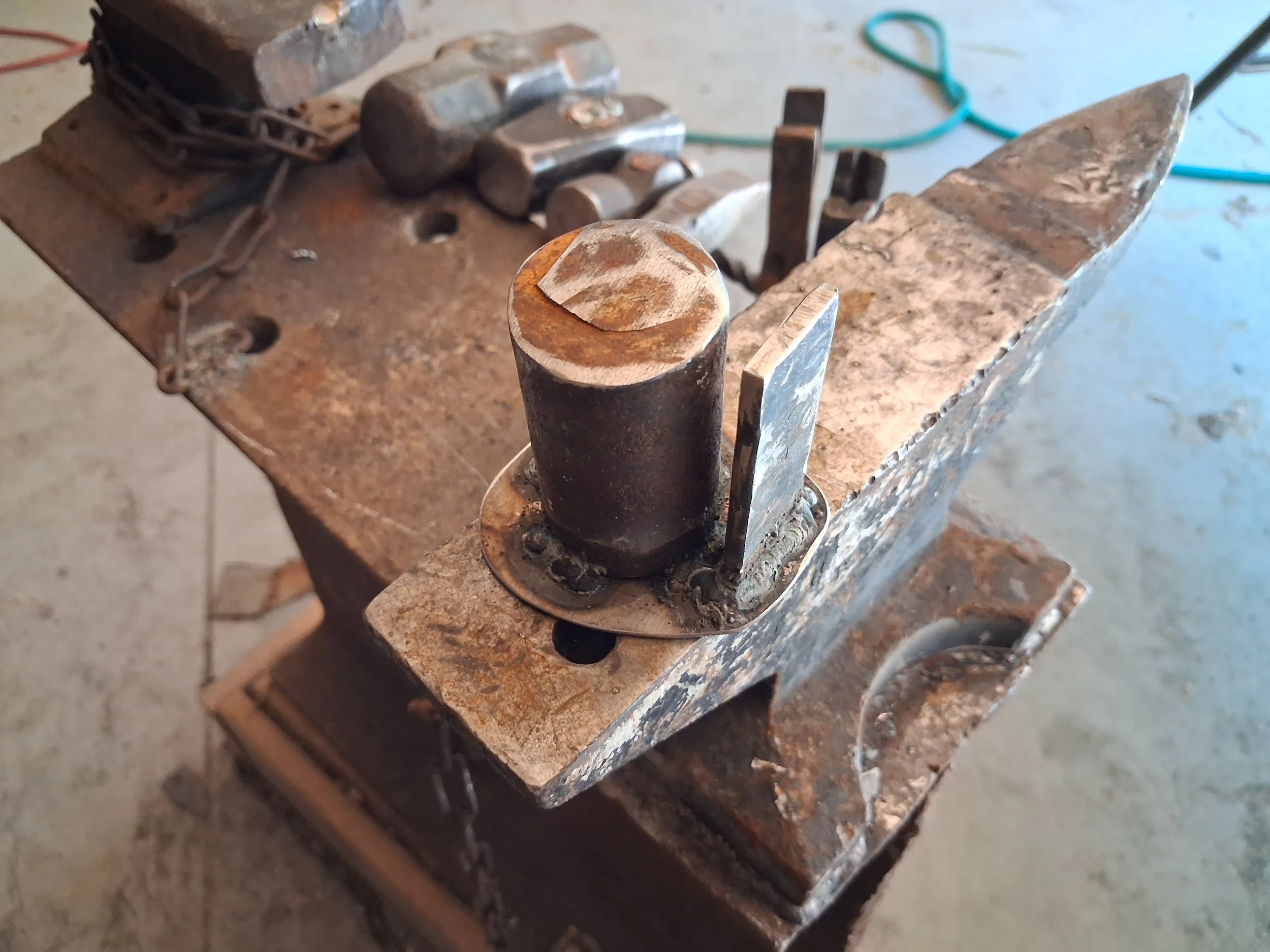 Close-up of a rusty metal machine part with a threaded bolt and various other metal components on a workbench.
