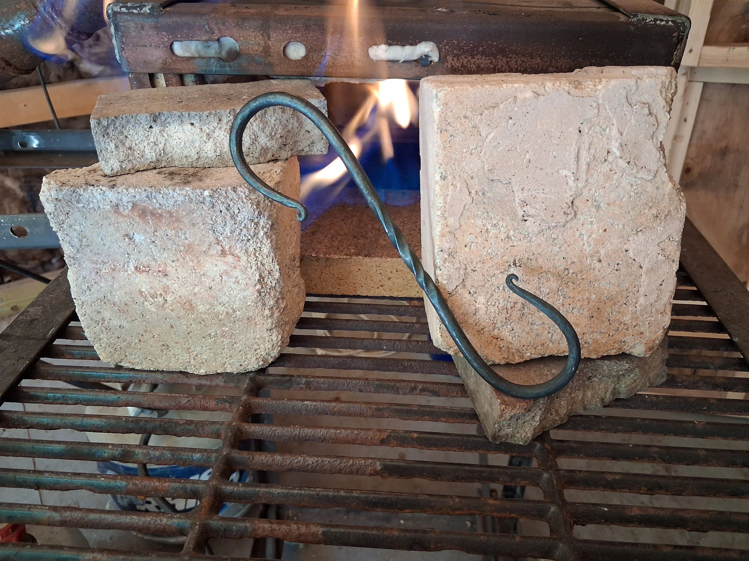 Bricks stacked with a metal tool inserted, blue flames underneath, on a metal grill.