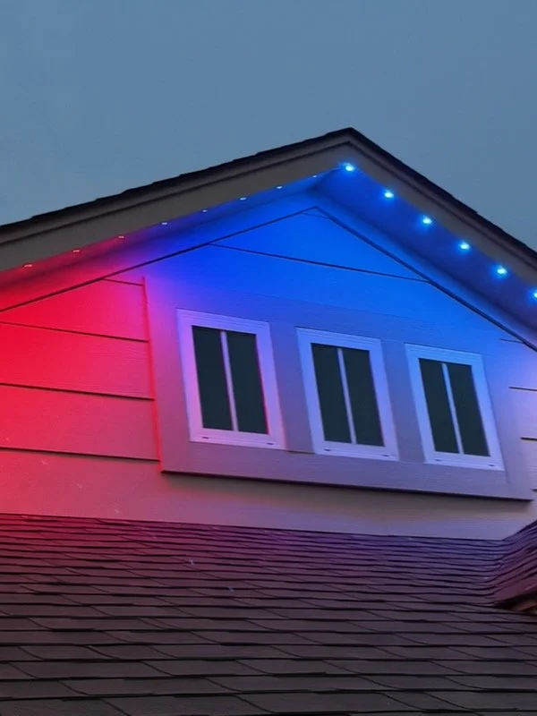Exterior of a house at dusk with blue and red neon lights on the roof and on the side of the house near the window.