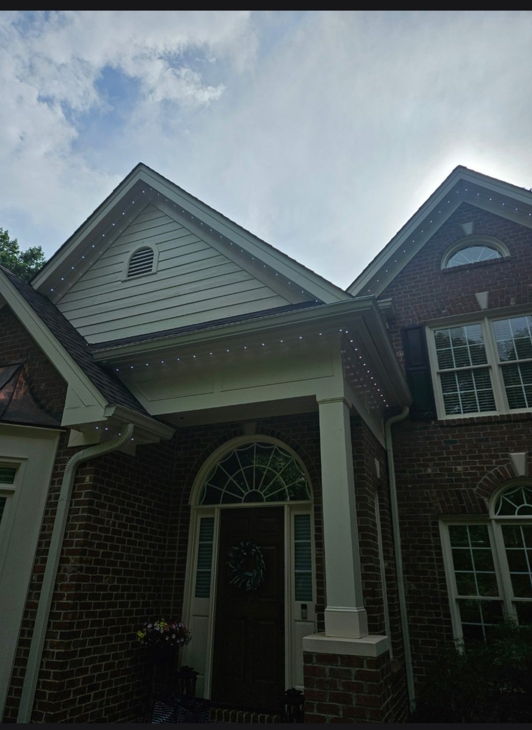 Front view of a brick house with white trim and a covered porch, decorated with Christmas wreath, under a partly cloudy sky.