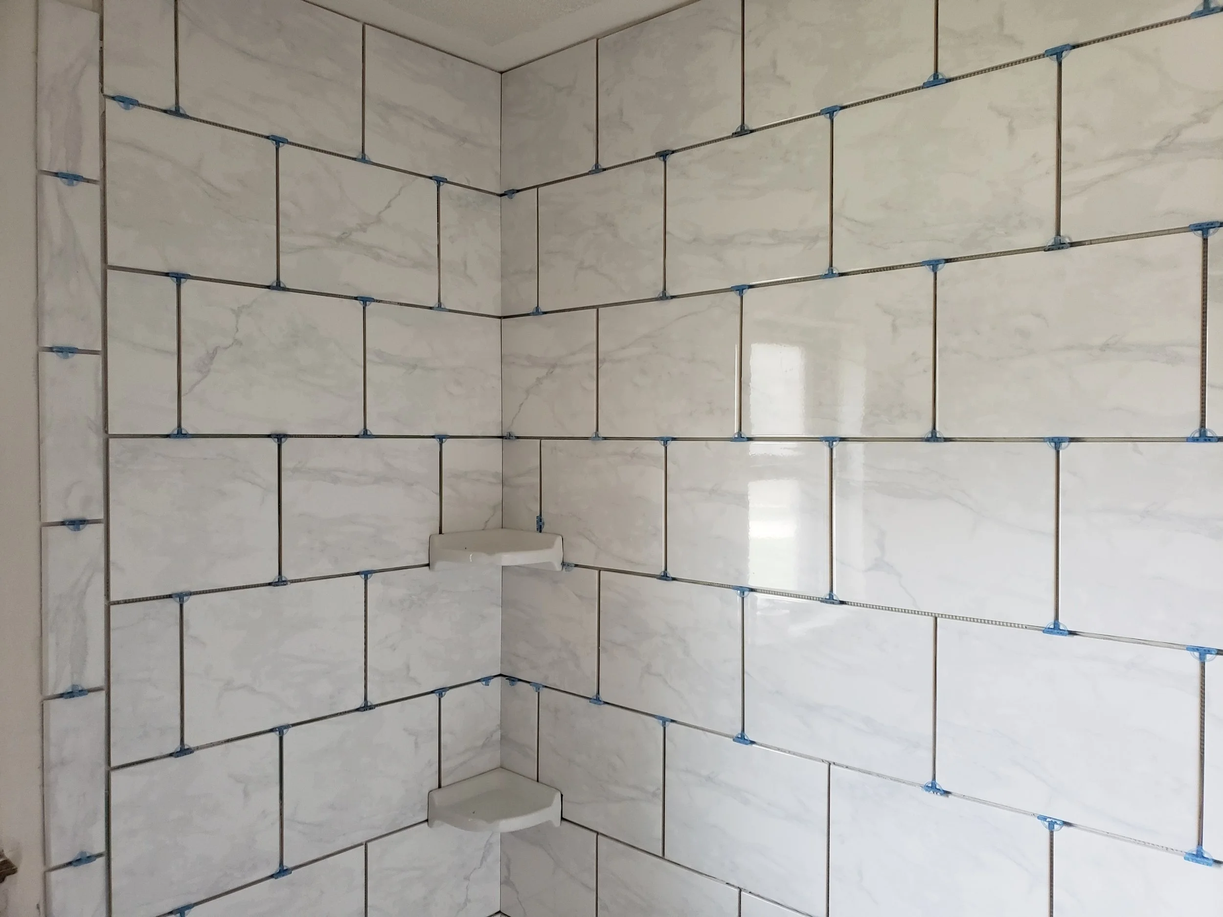 Tiled wall with tiles being installed using spacers and a small soap dish in the corner.