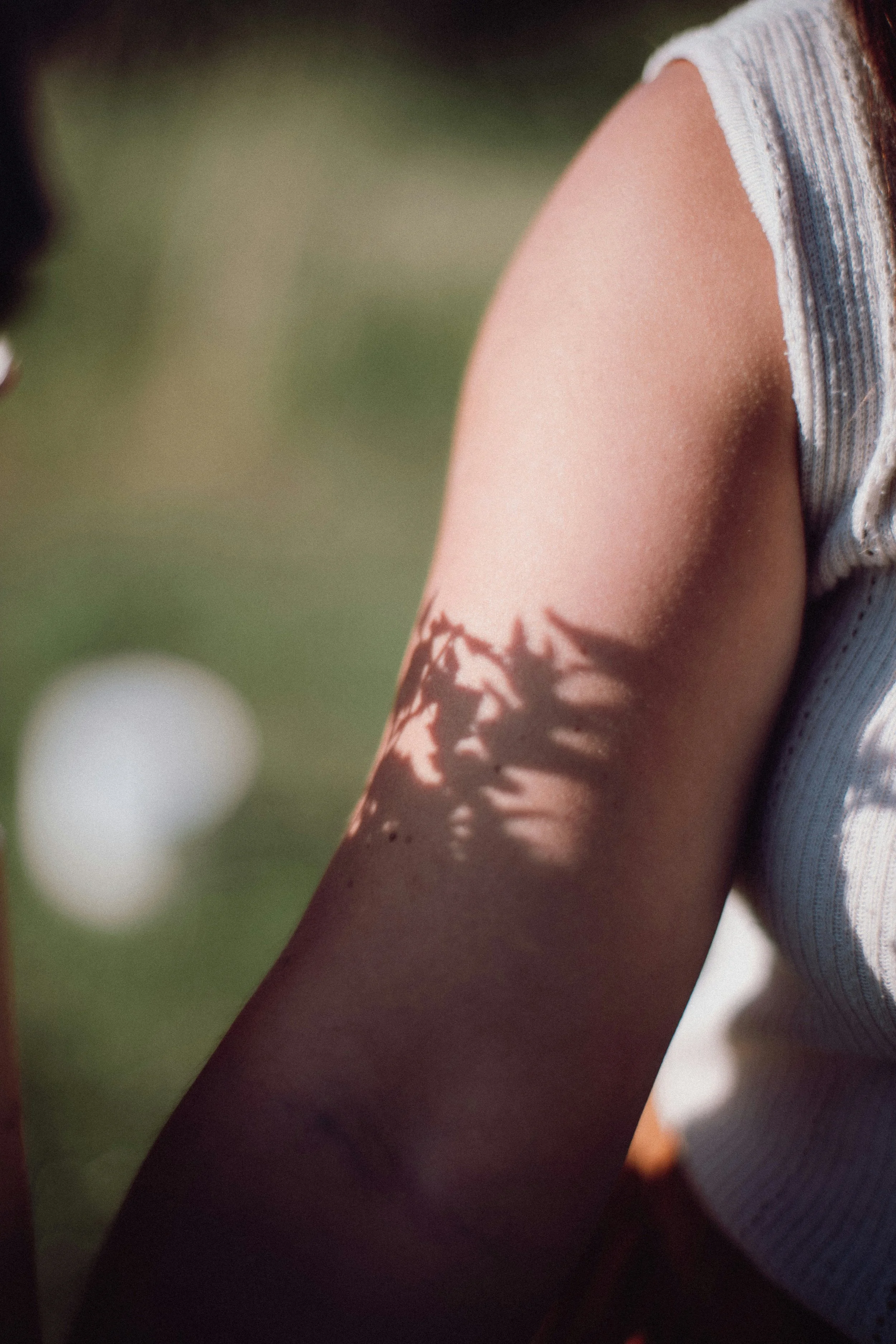 Brazo de una mujer con sombras de hojas proyectadas sobre la piel.