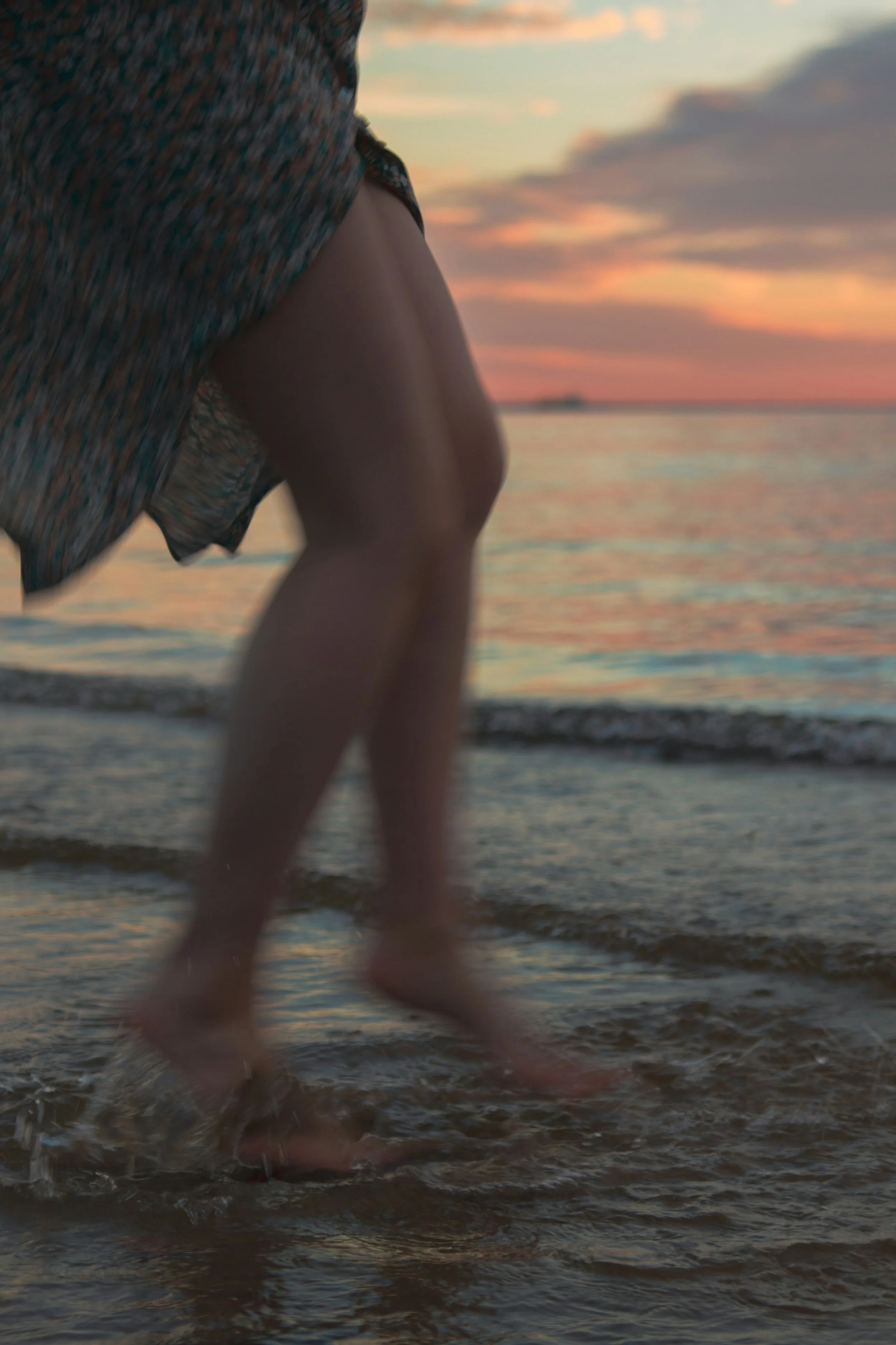 Mujer en movimiento en la orilla del mar tocando el agua con los pies.