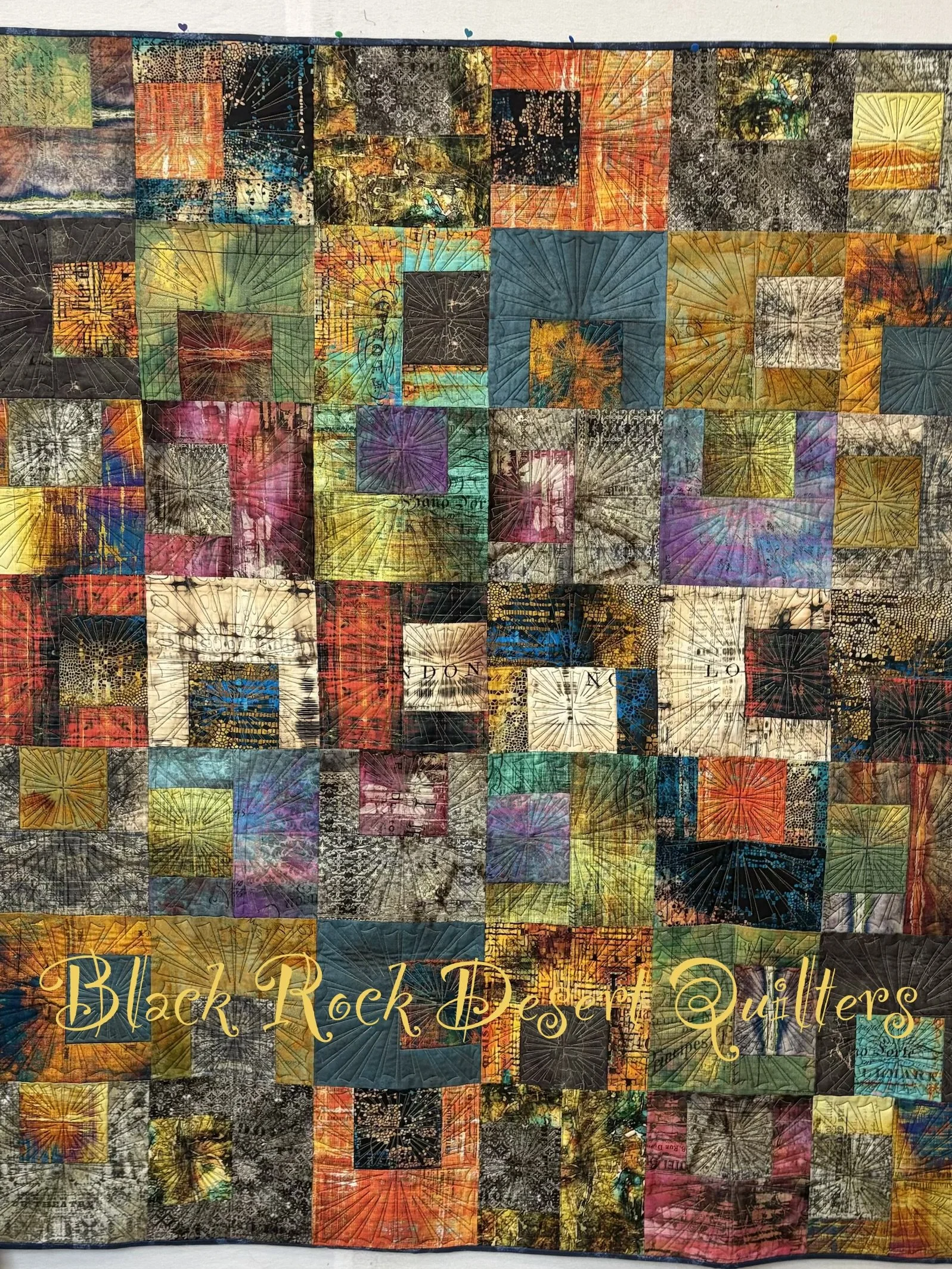 A colorful quilt made of patchwork squares with various patterns and colors, with the text 'Black Rock Deser Quilters' written in gold at the bottom.