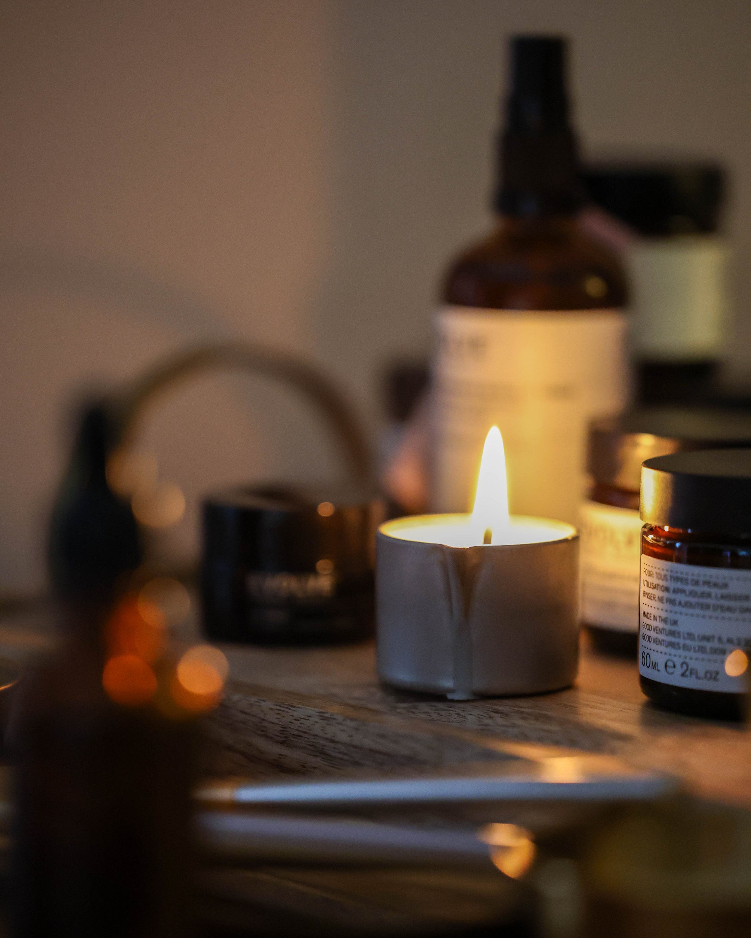 Blurred close-up of a lit candle surrounded by amber essential oil bottles on a wooden surface.