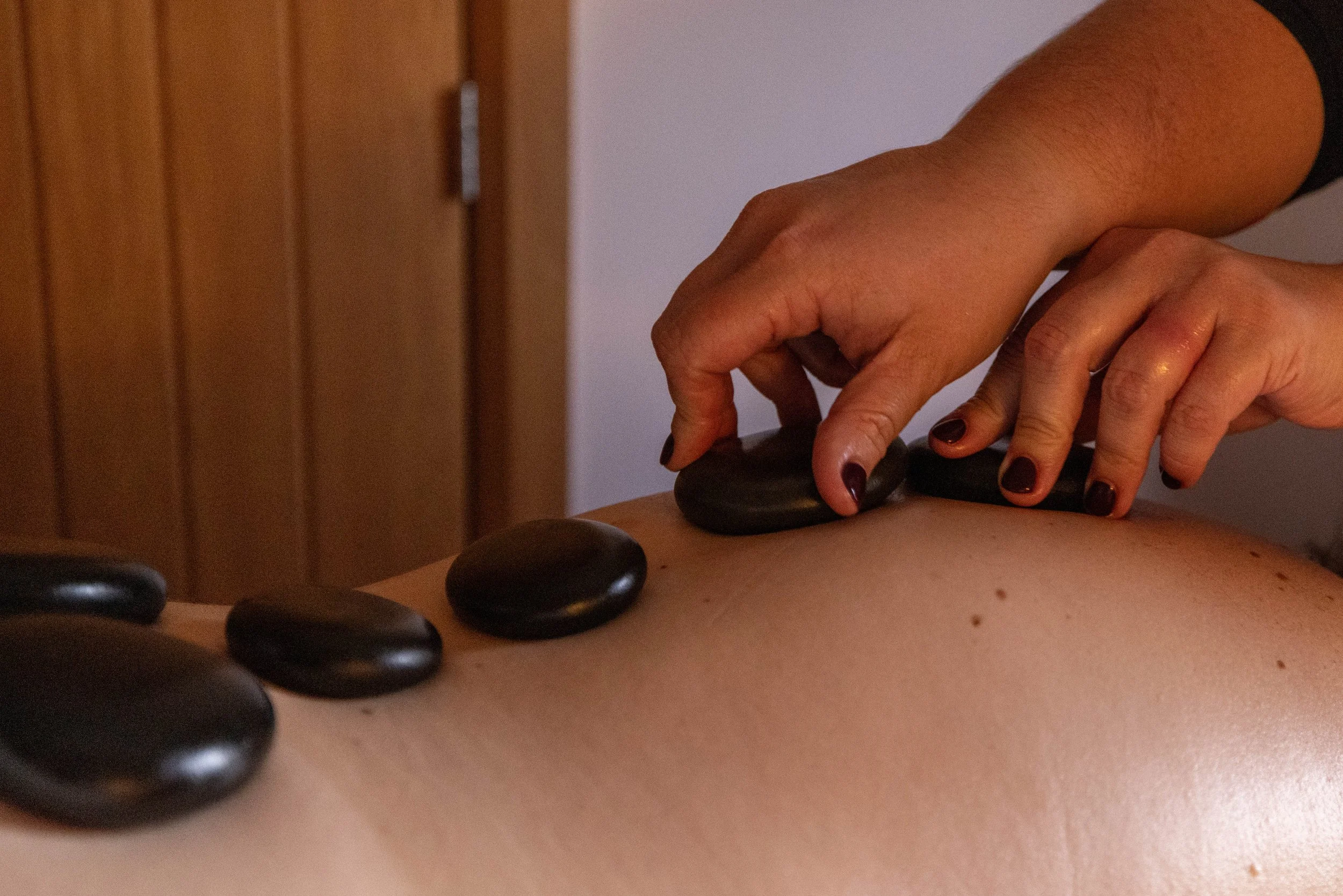 Hands with dark nail polish arranging smooth black stones on a wooden surface