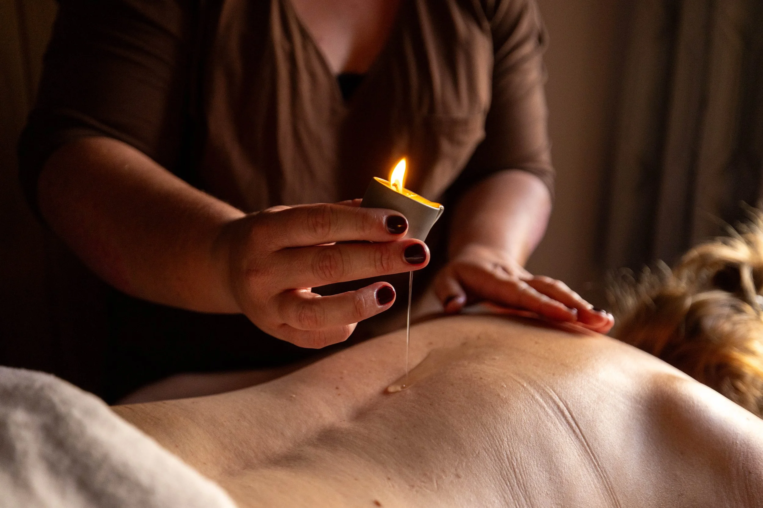Massage therapist holding a lit candle while performing a relaxing spa treatment