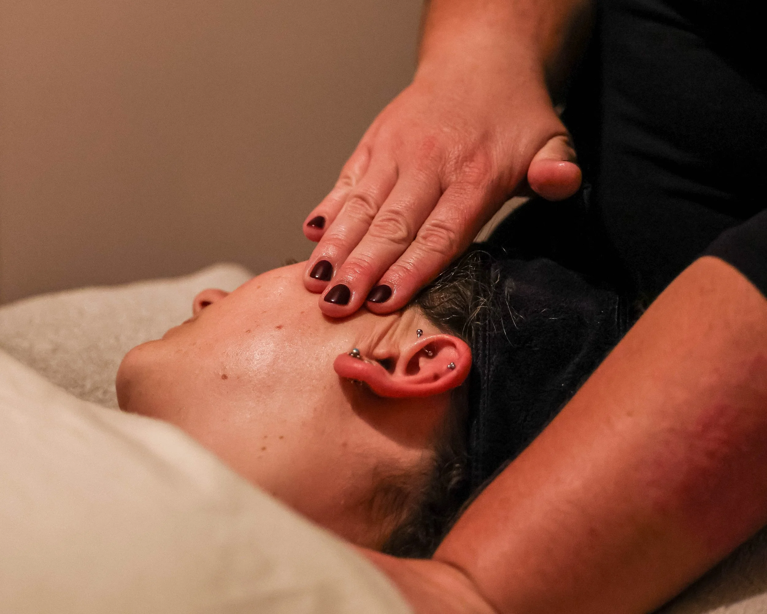 Close-up of a person receiving a shoulder massage, with the therapist’s burgundy-polished hand resting on their shoulder.