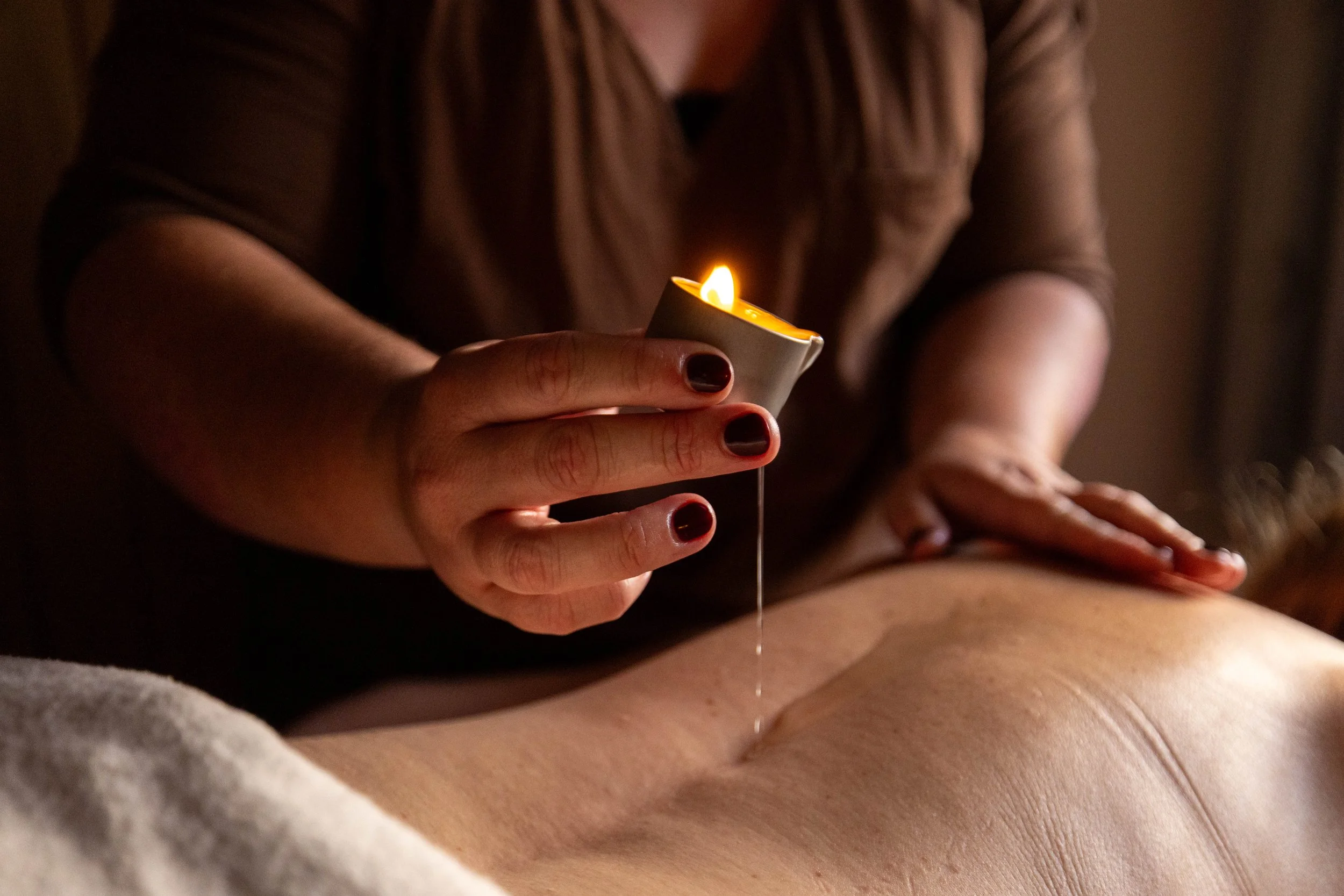 Close-up of a massage therapist holding a lit candle over a client's back during a candle massage