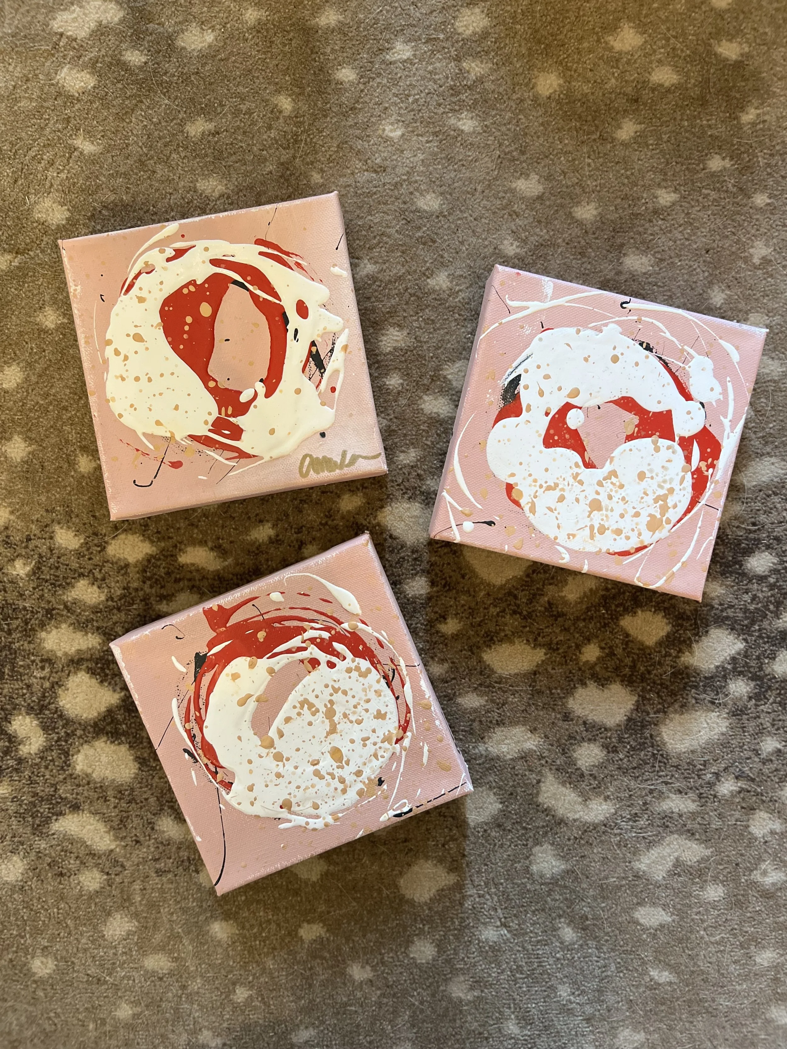 Three small pink canvases with abstract art featuring white, red, and blue splashes.