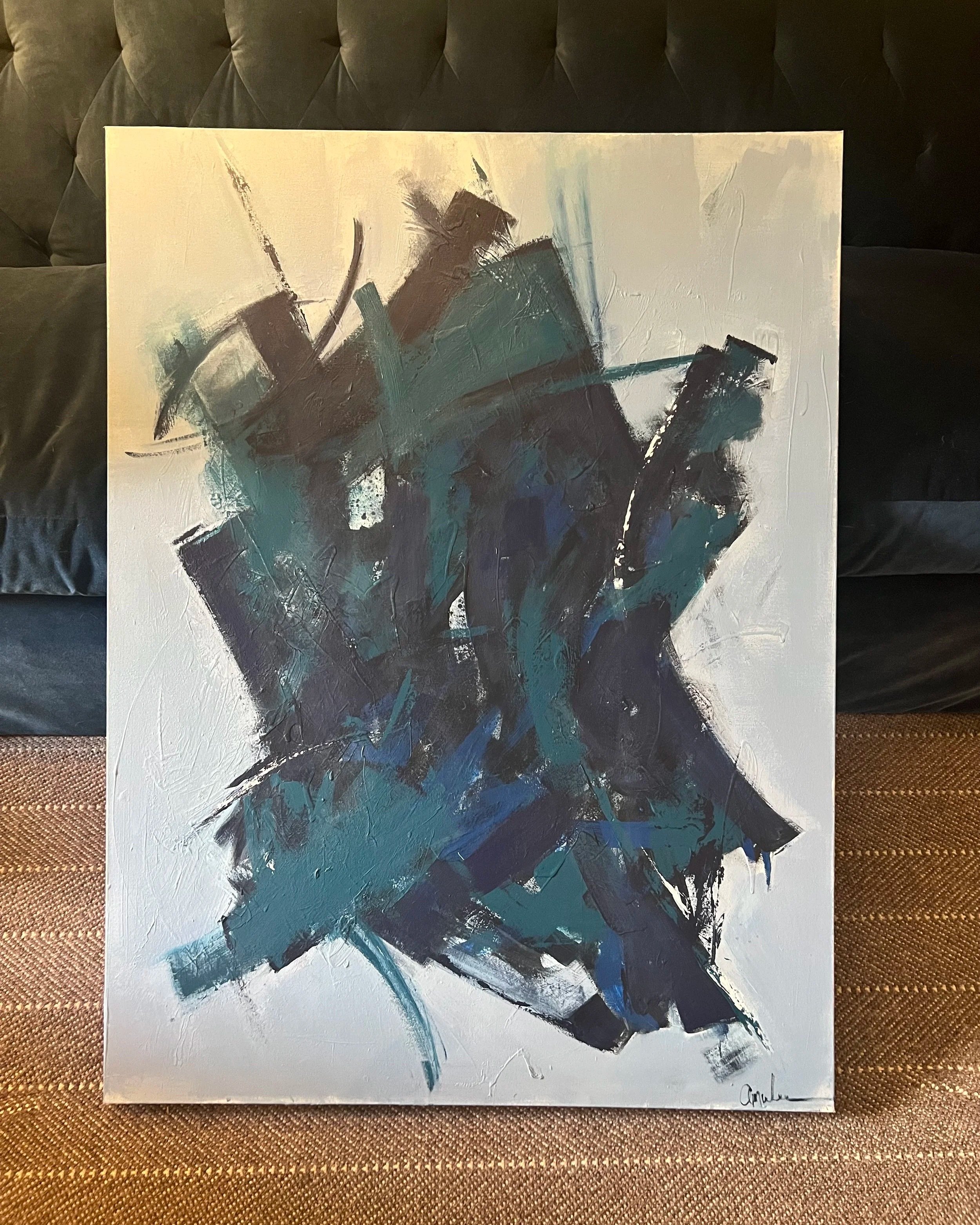 Abstract painting with bold brushstrokes in shades of navy, teal, and white, propped against a navy velvet sofa.