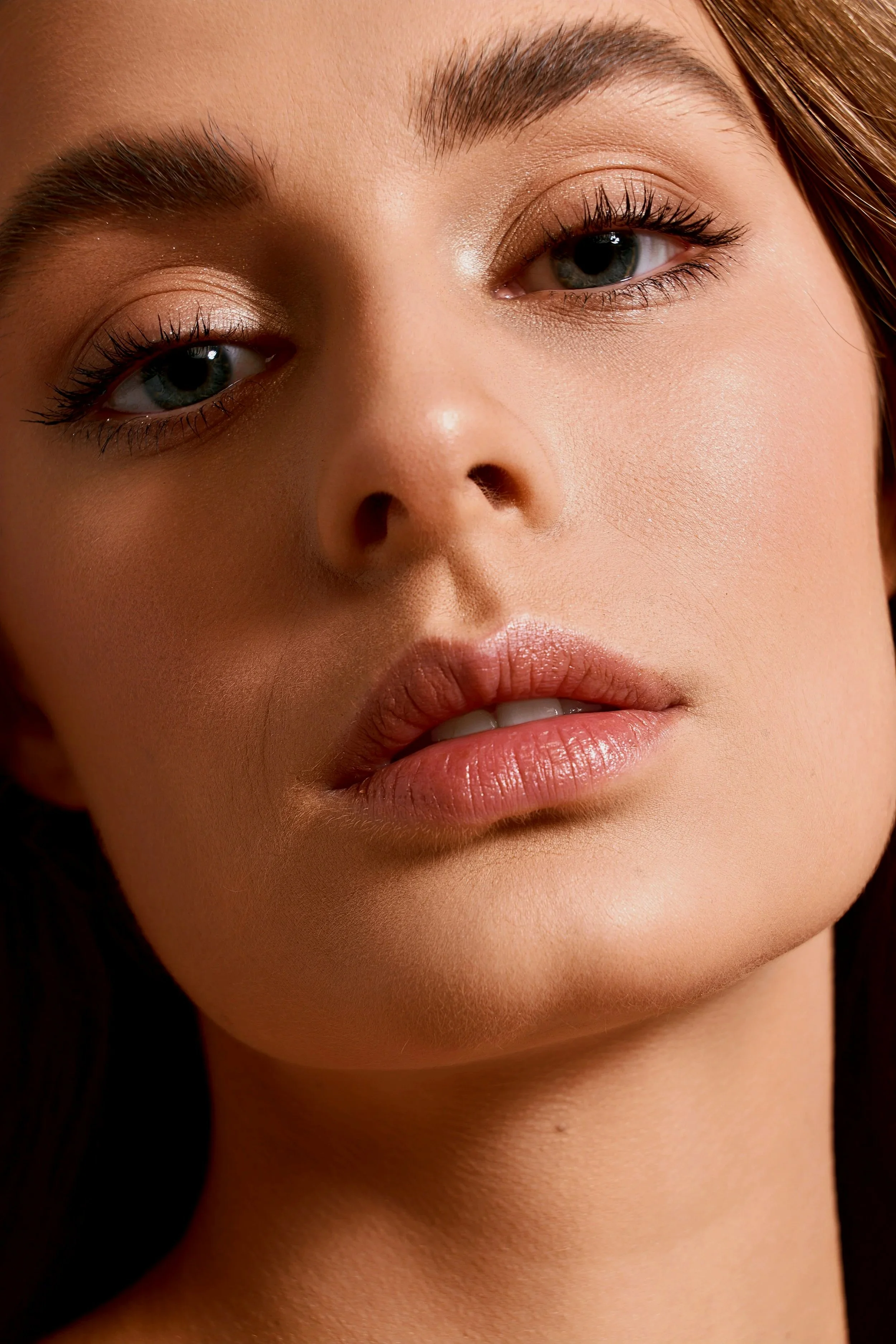 Close-up of a woman's face, highlighting her blue eyes, eyebrows, and lips with smooth skin and natural makeup.