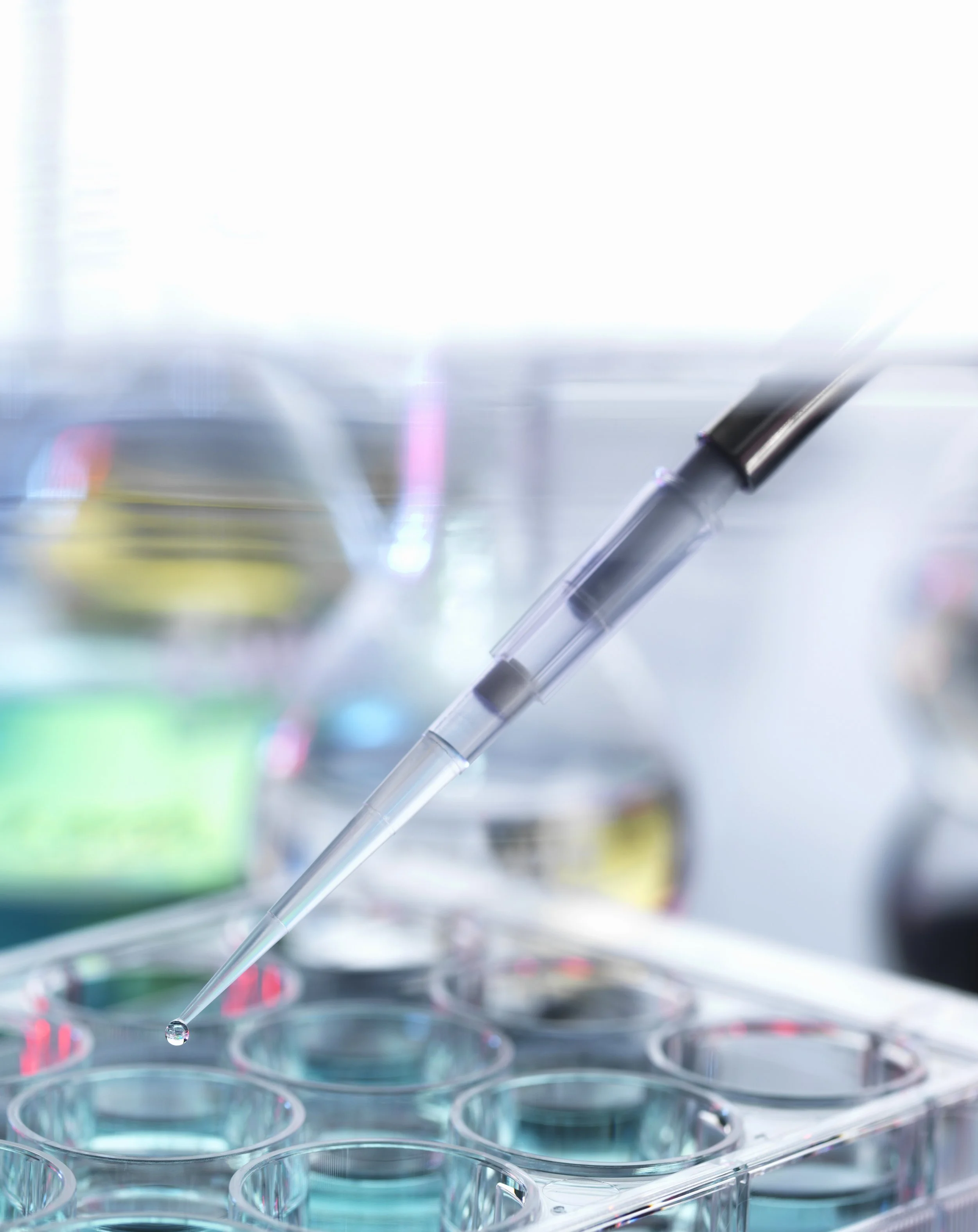 Close-up of a pipette dispensing liquid into a row of test tubes with colored liquids.