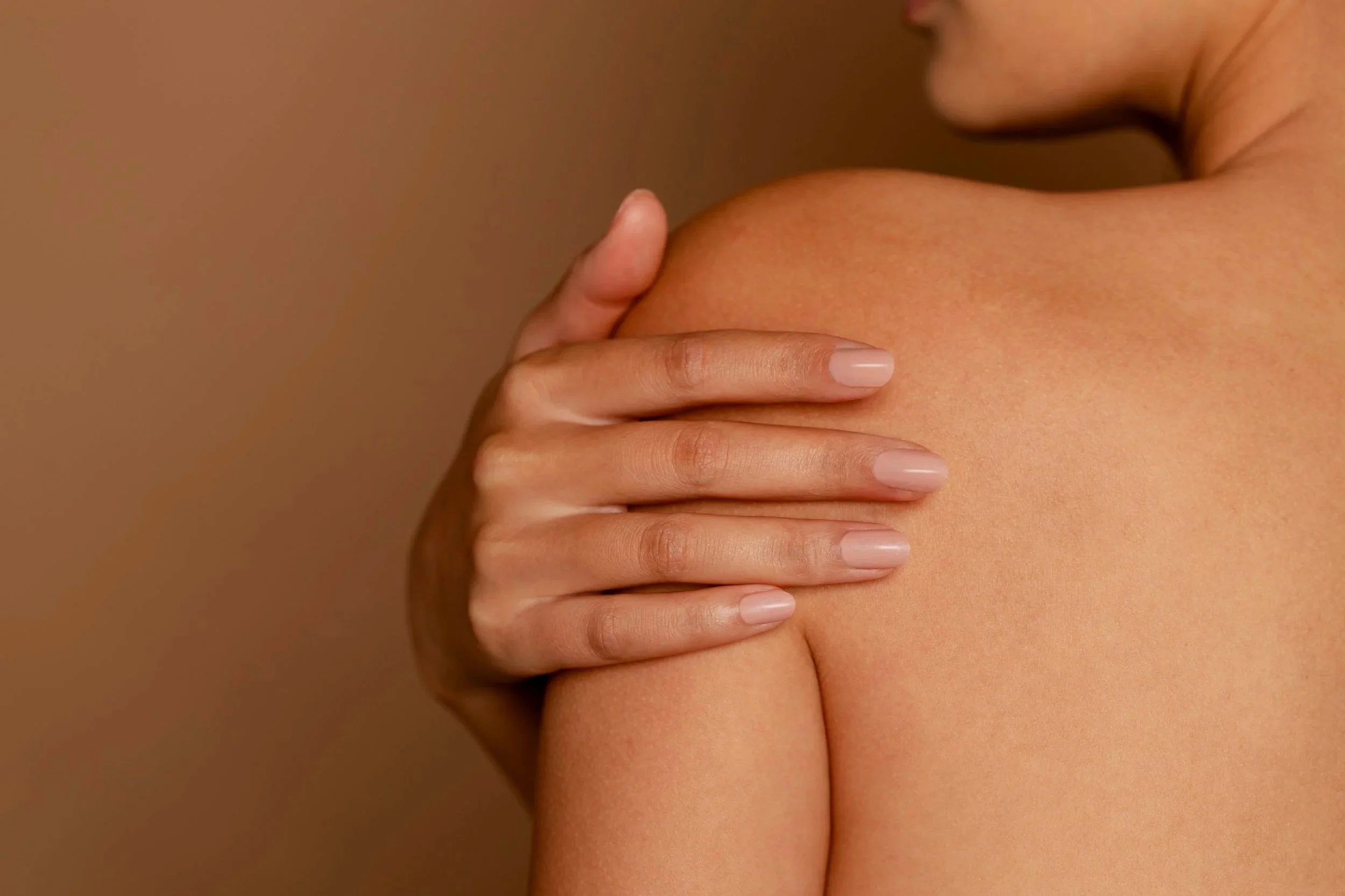 Close-up of a person's hand gently touching their shoulder and part of their face, with smooth skin and natural lighting.