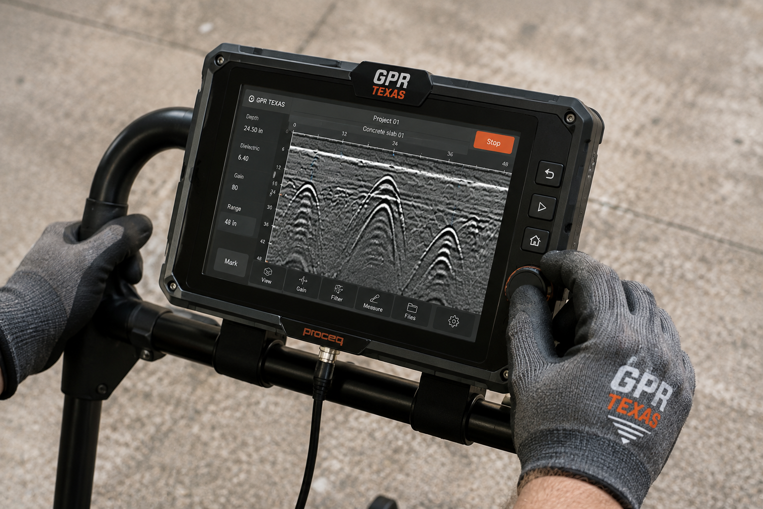 Person operating a GPR (ground-penetrating radar) device on a concrete surface, with gloves bearing the GPR Texas logo.