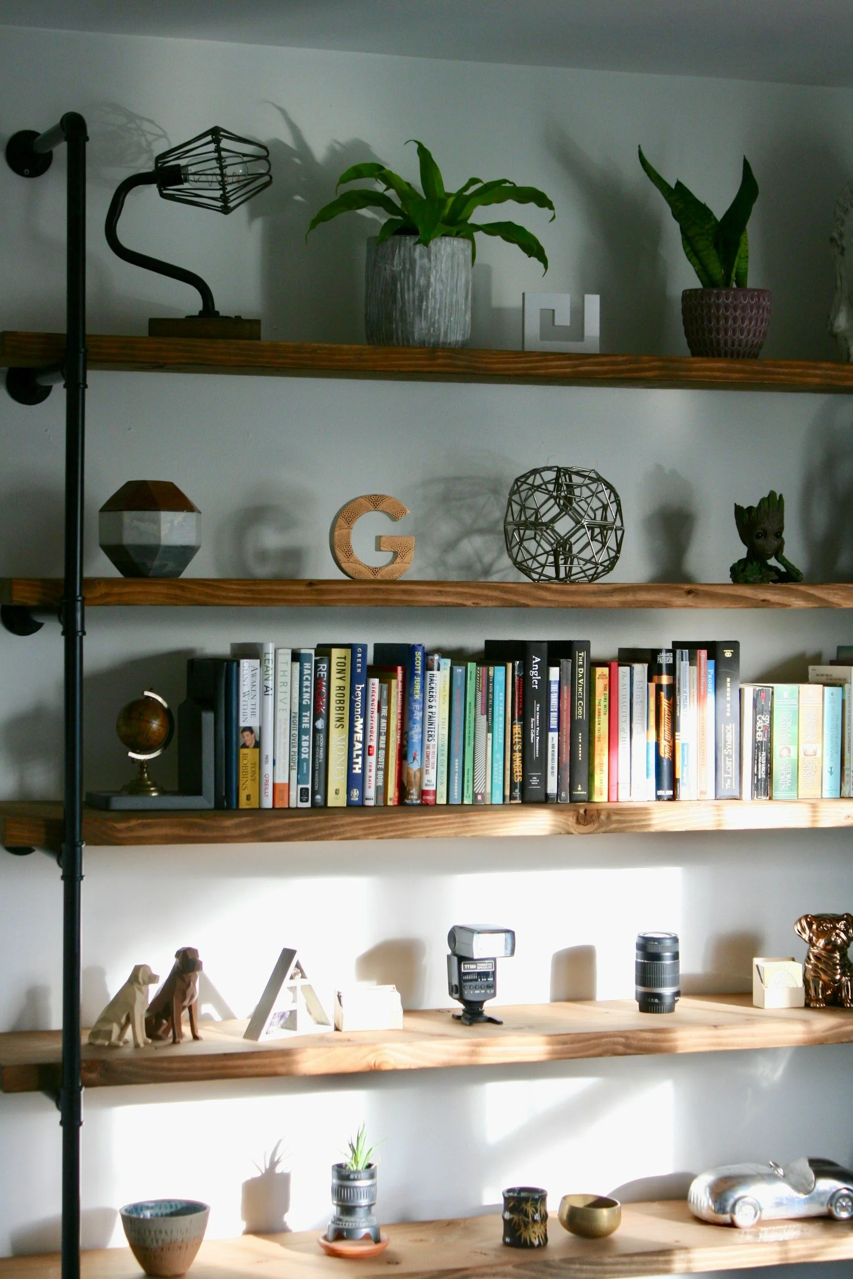 A wooden bookshelf with three shelves containing decorative items, plants, books, and various objects.