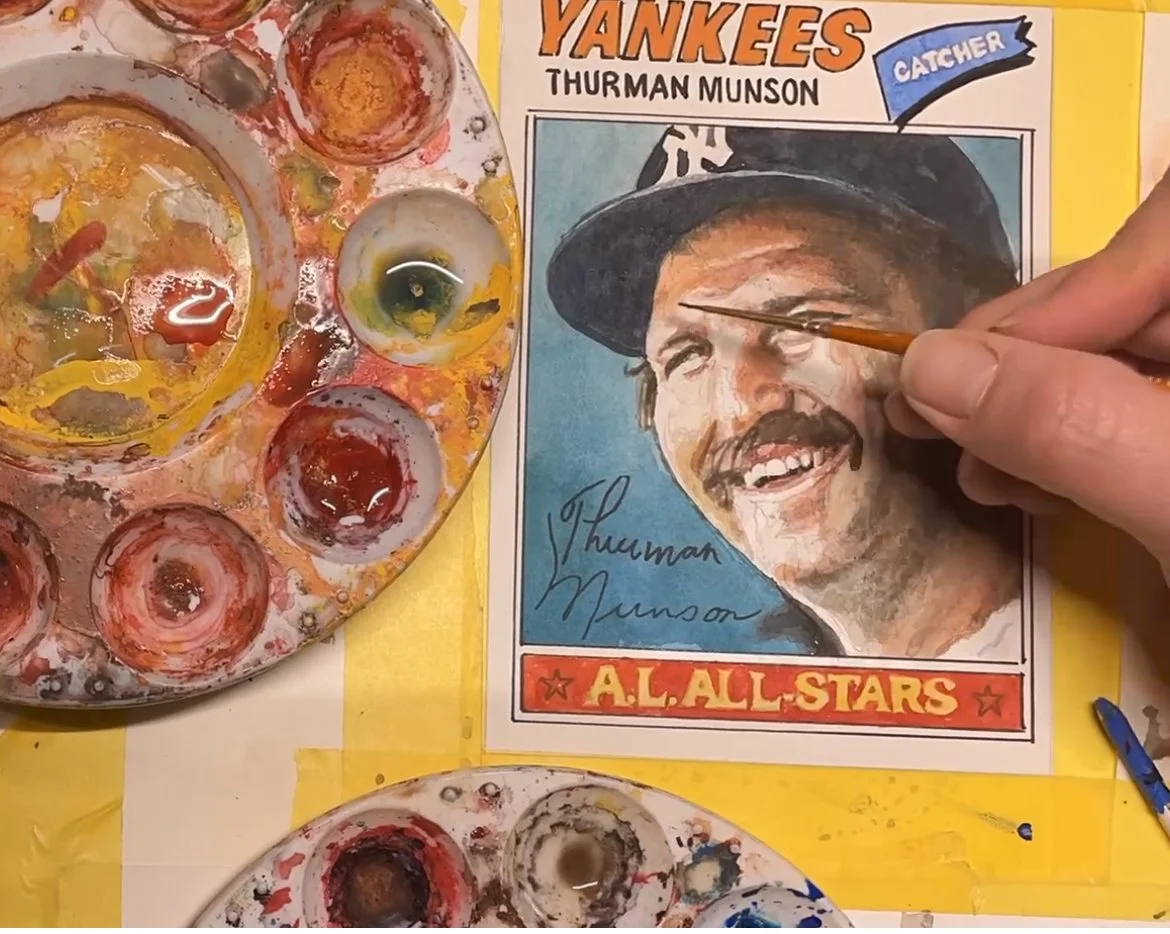 An artist painting a colorful portrait of Thurman Munson, a New York Yankees catcher, with a paint palette and brushes on a yellow surface.