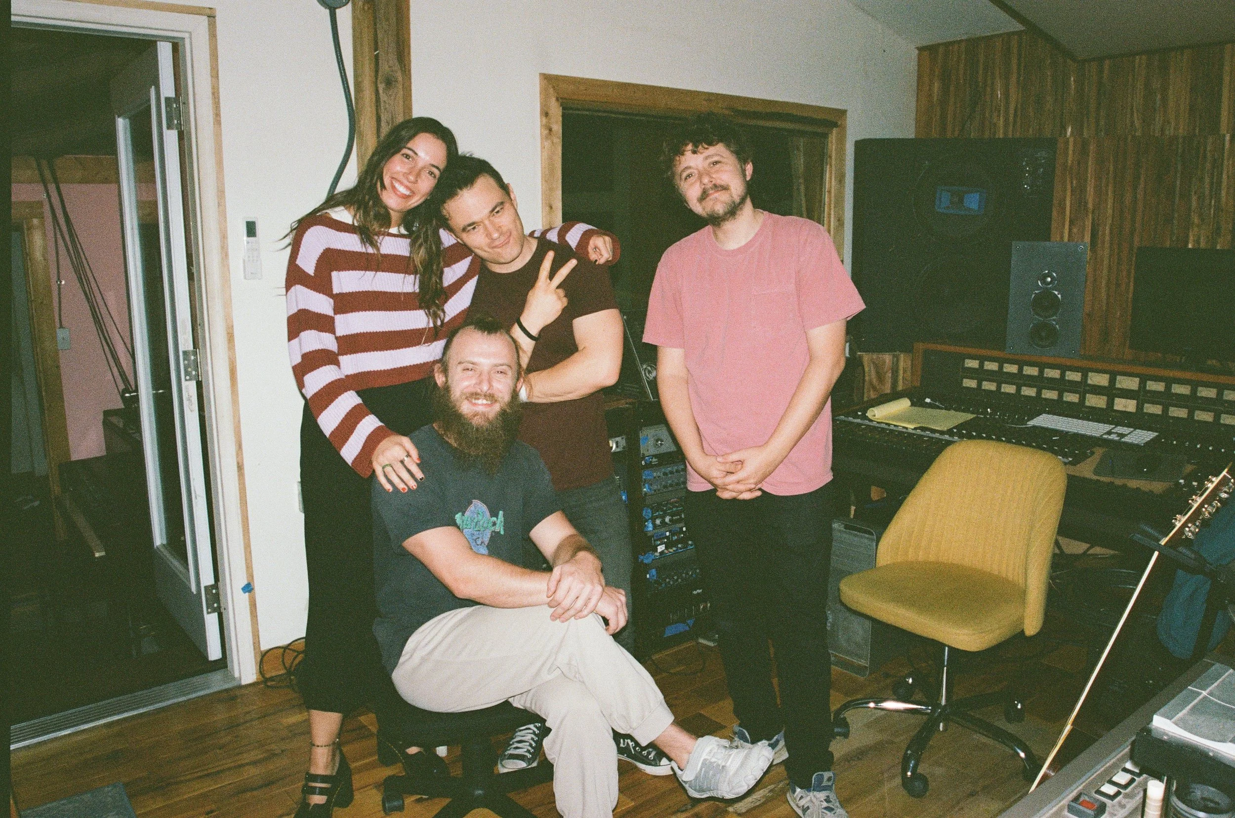 Group of five young adults in a music recording studio, smiling and posing for the photo. Music being recorded at The Bomb Shelter Studios.