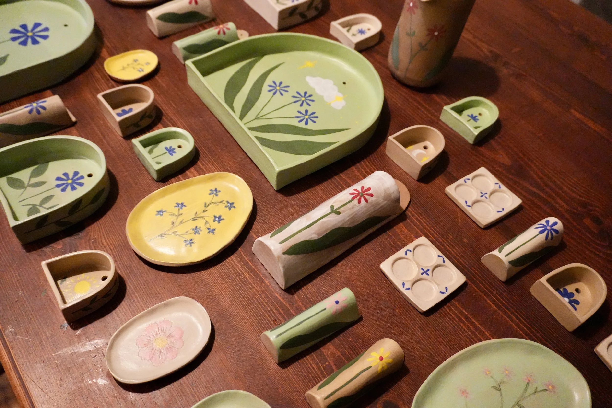 Various painted ceramic dishes and objects decorated with floral and nature motifs, placed on a wooden surface.