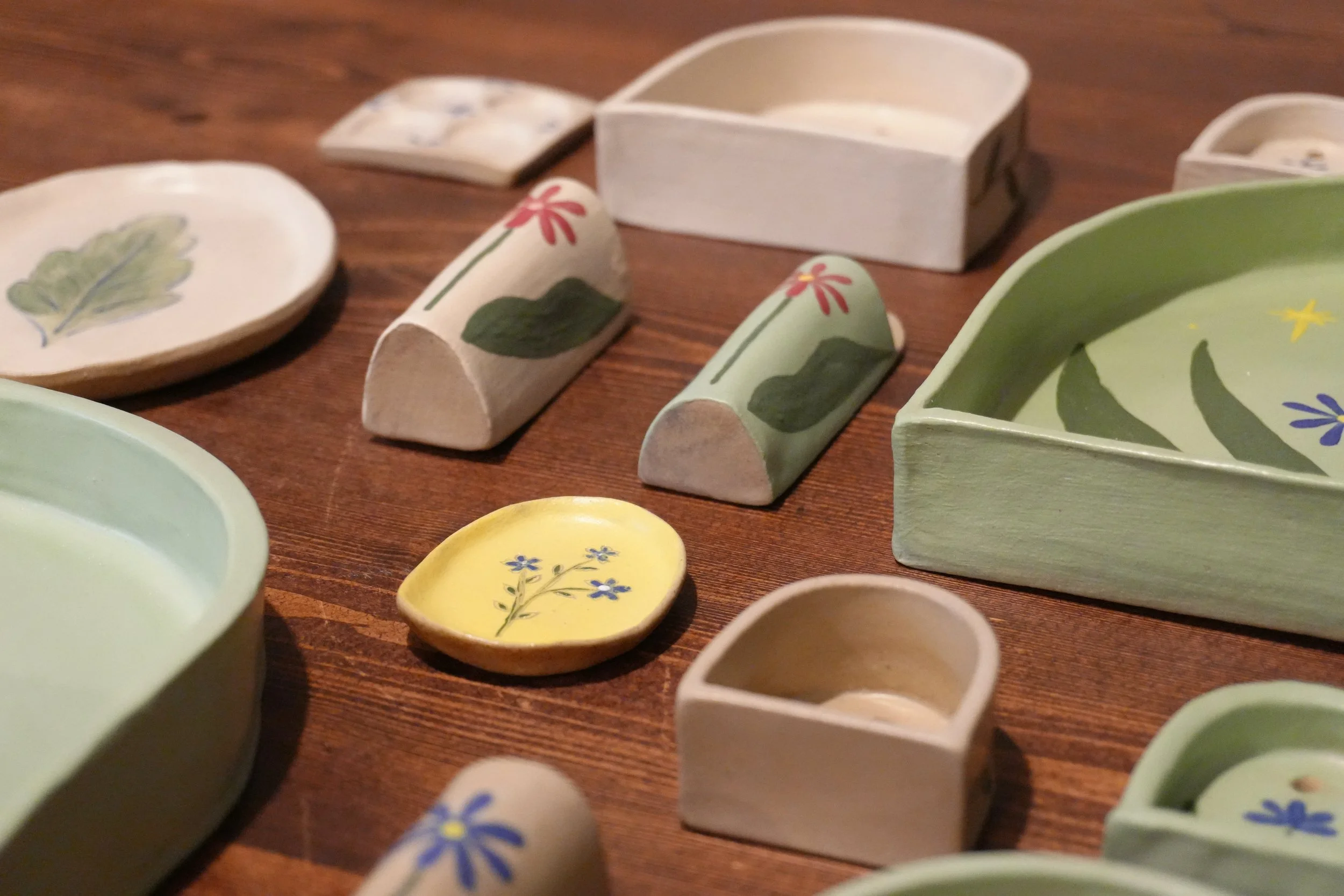Various small hand-painted ceramics with floral and leaf designs on a wooden surface.