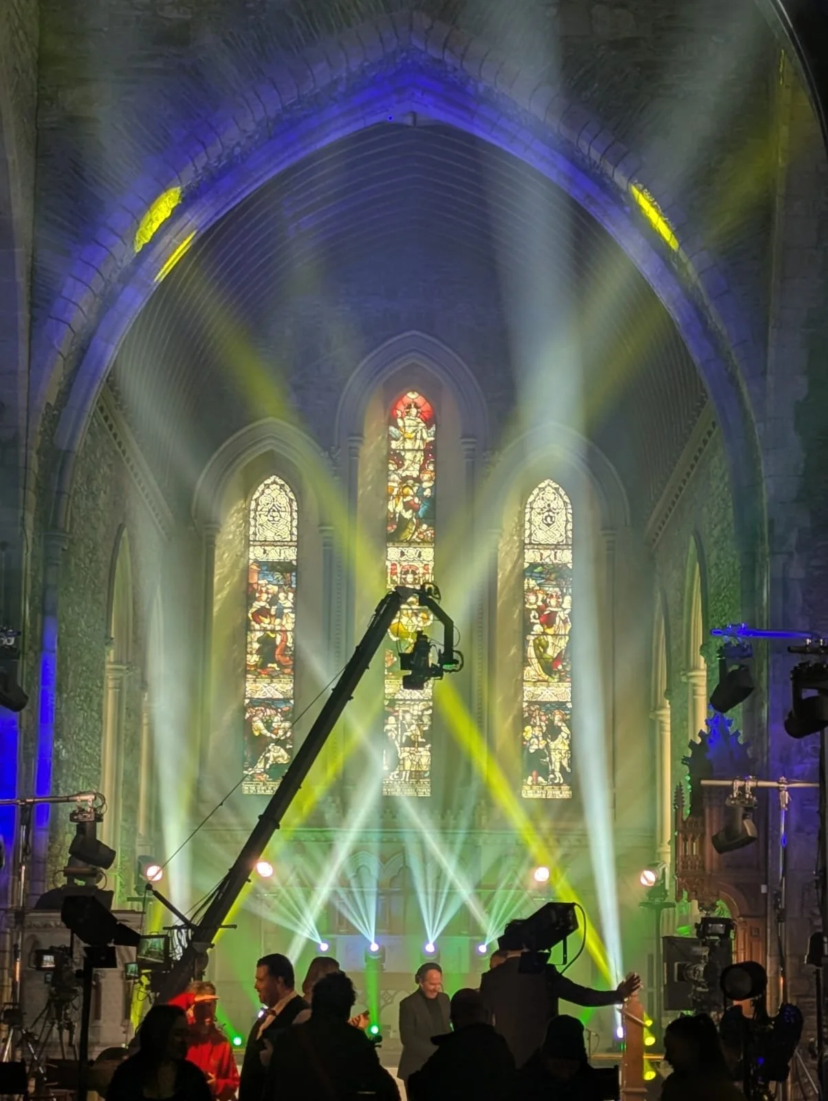 Inside a church with stained glass windows, colorful stage lighting, and people enjoying an event.