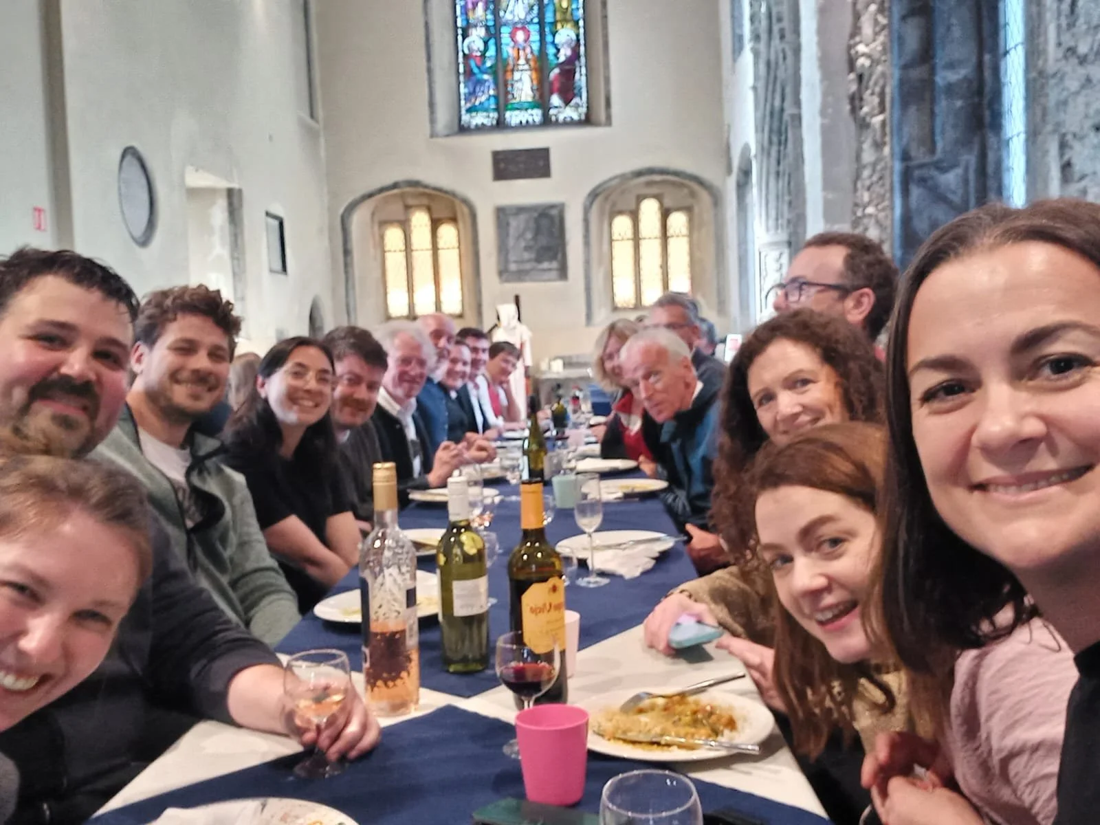 A large group of people gathered around a long dinner table inside a decorated church, celebrating with food and drinks.