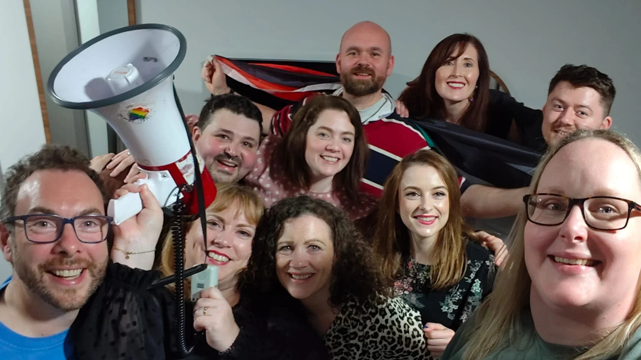 Group of smiling people in a close-up photo, some holding a megaphone, celebrating together at a gathering.