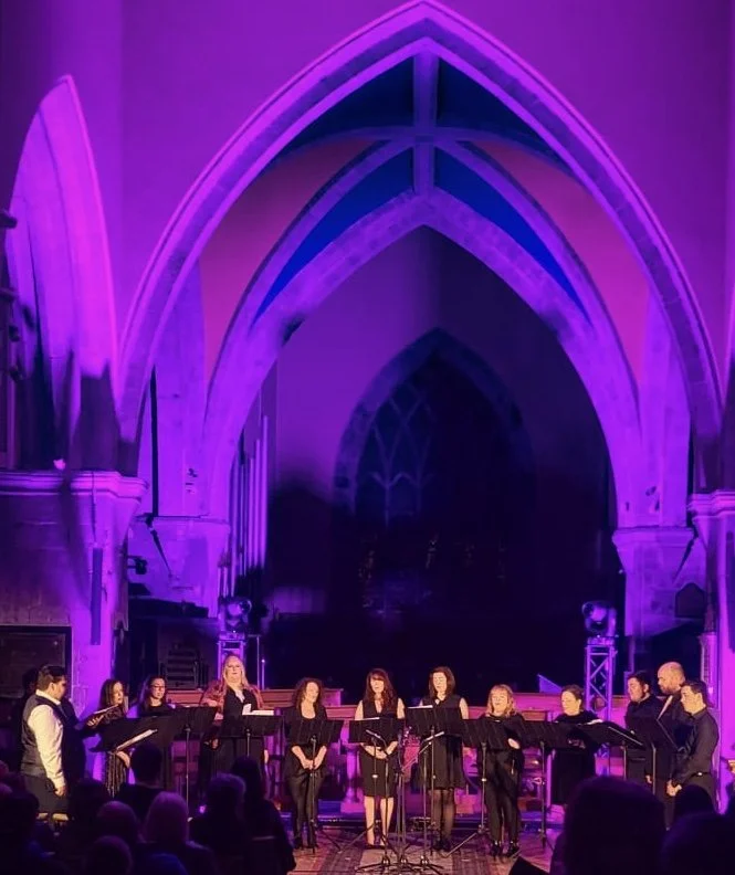Choir performing on stage inside a cathedral illuminated with purple lighting.