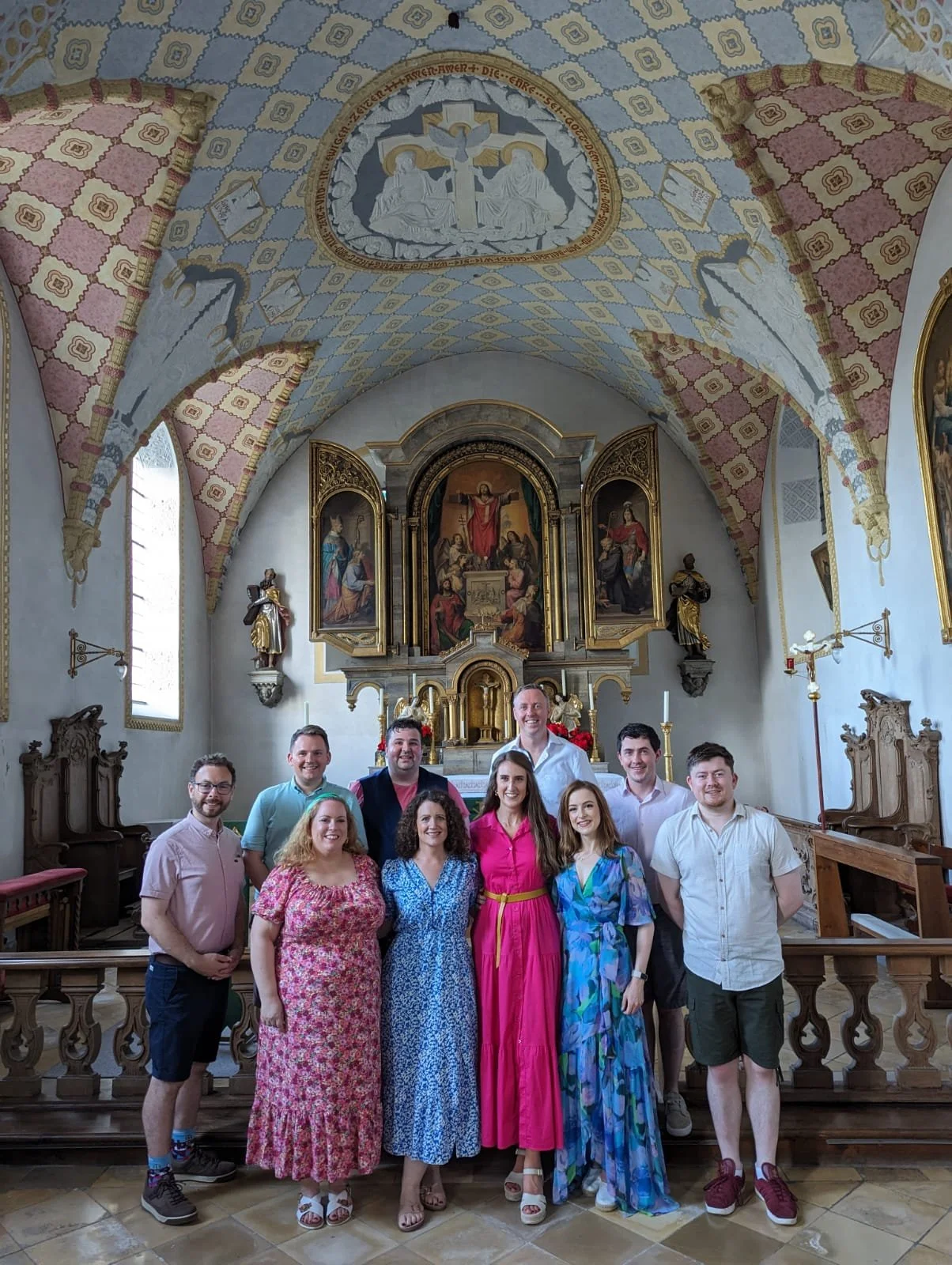 Group of nine people standing inside a church in front of an altar, with decorative paintings, statues, and a religious iconography on the wall and ceiling.