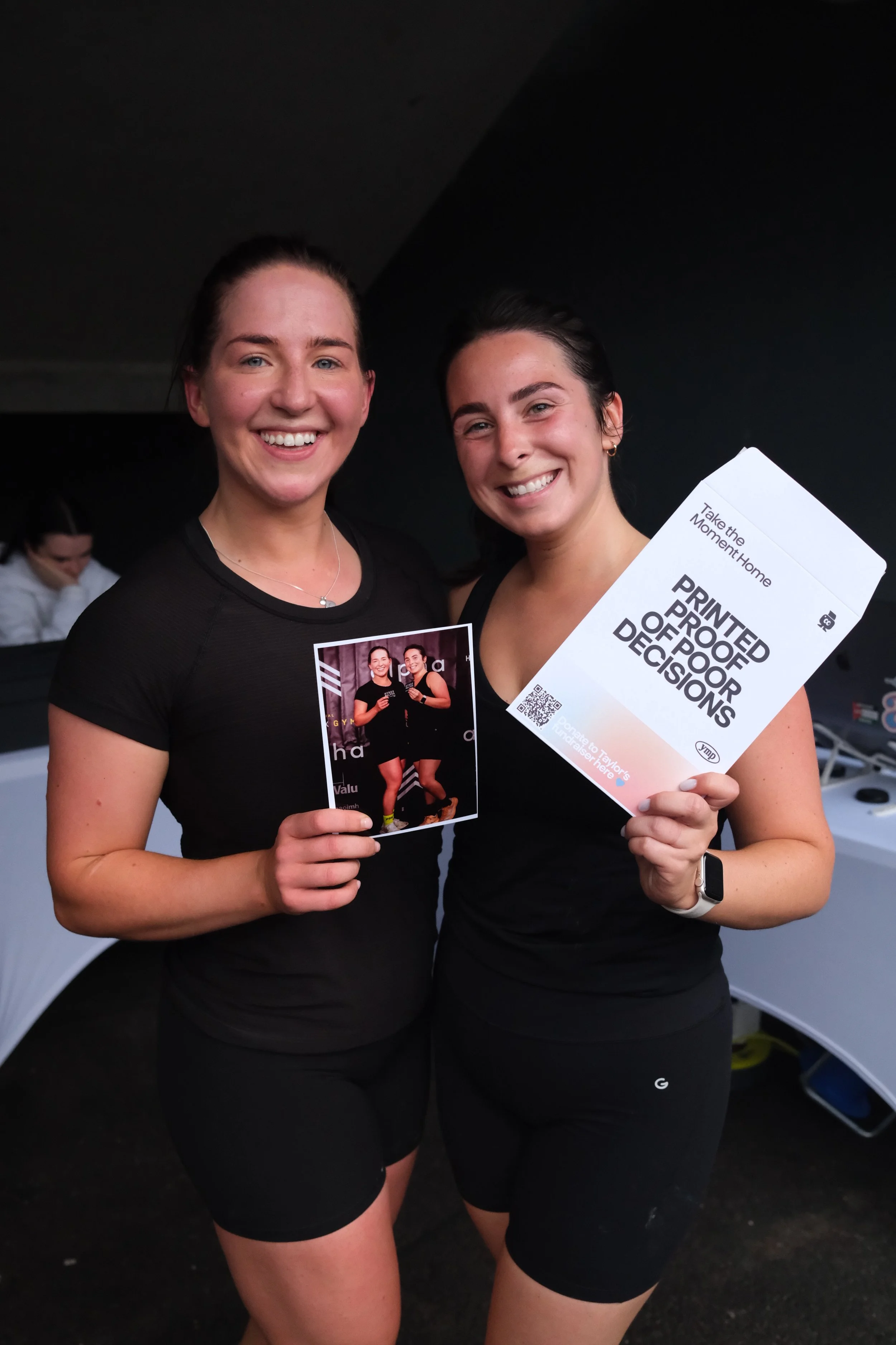 Two finishers smiling with their instant print and envelope