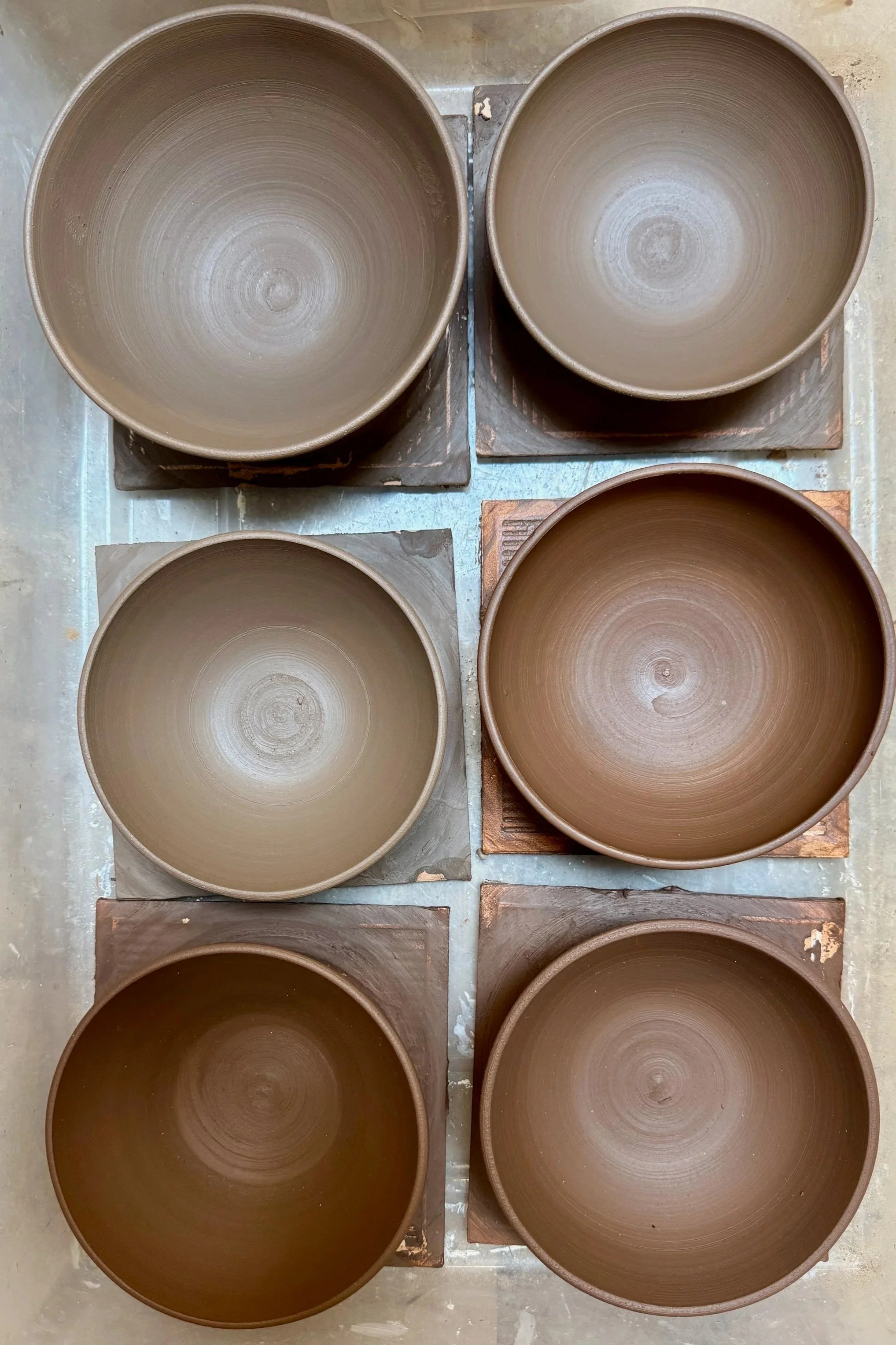 Six unfired clay pots, arranged in two rows of three, with brown color and concentric circle patterns inside.