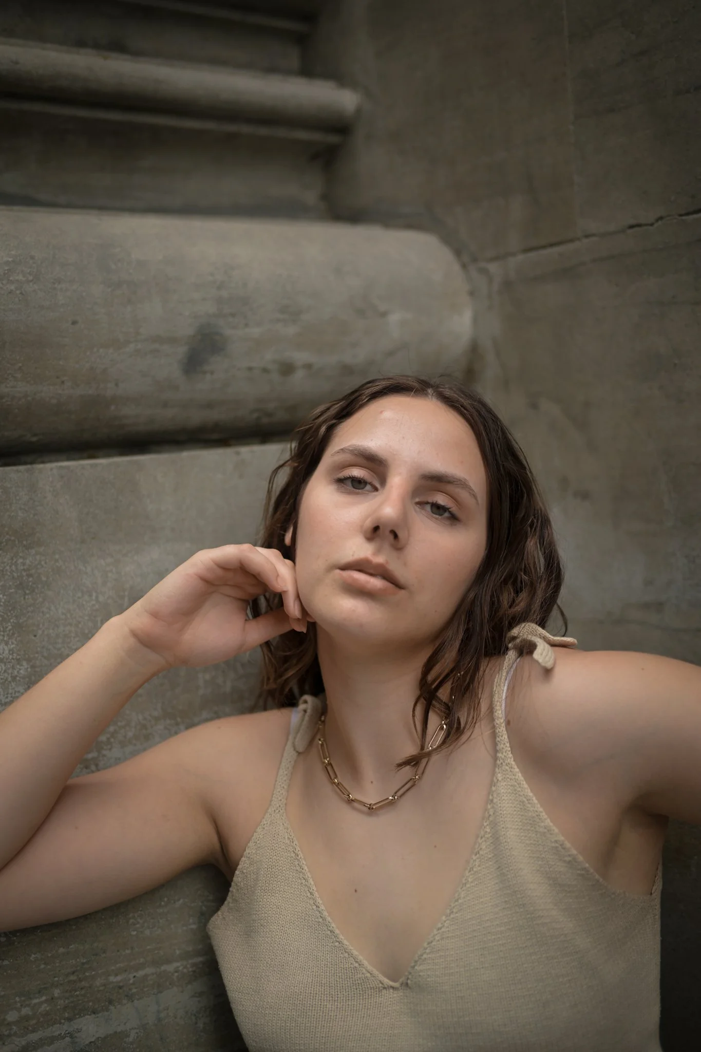 A young woman with wavy brown hair and light skin taking a selfie while lying on the ground in front of a concrete staircase.