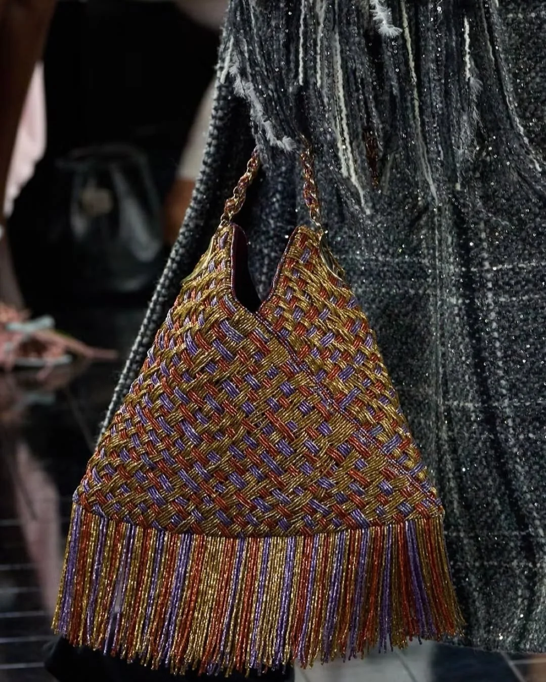 A colorful woven handbag with fringe, hanging from a person's arm, against a sparkly black jacket.