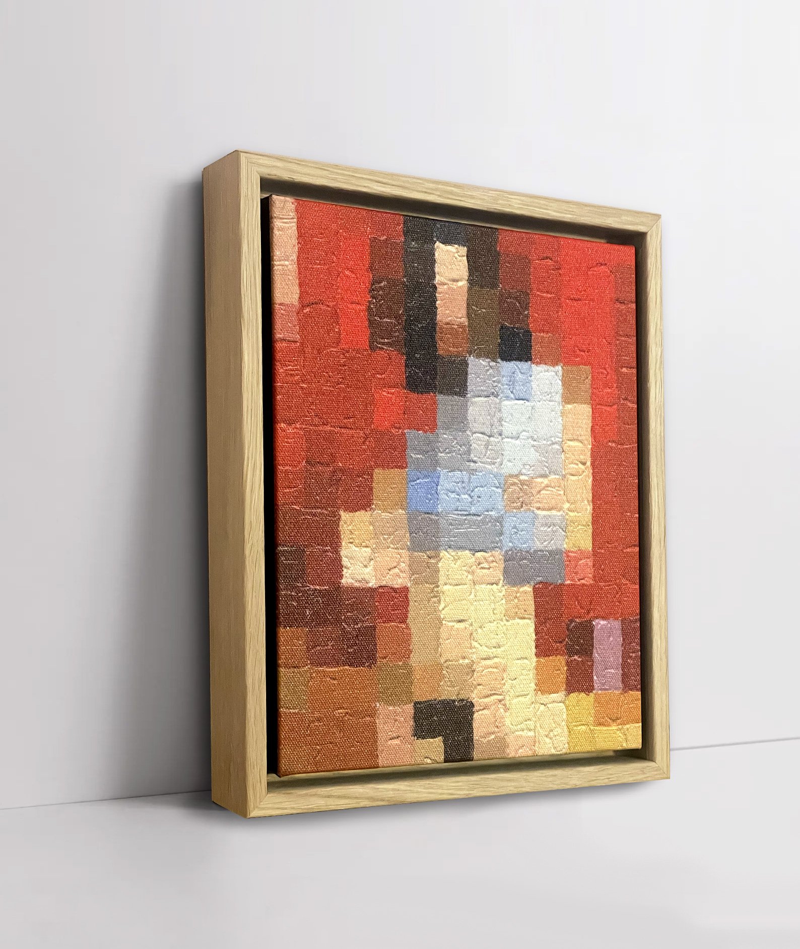 Framed pixellated painting of a nude woman, mainly in reds, browns, and blues, framed and mounted against a white wall.