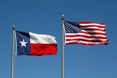Texas state flag and United States flag waving in the wind against a blue sky