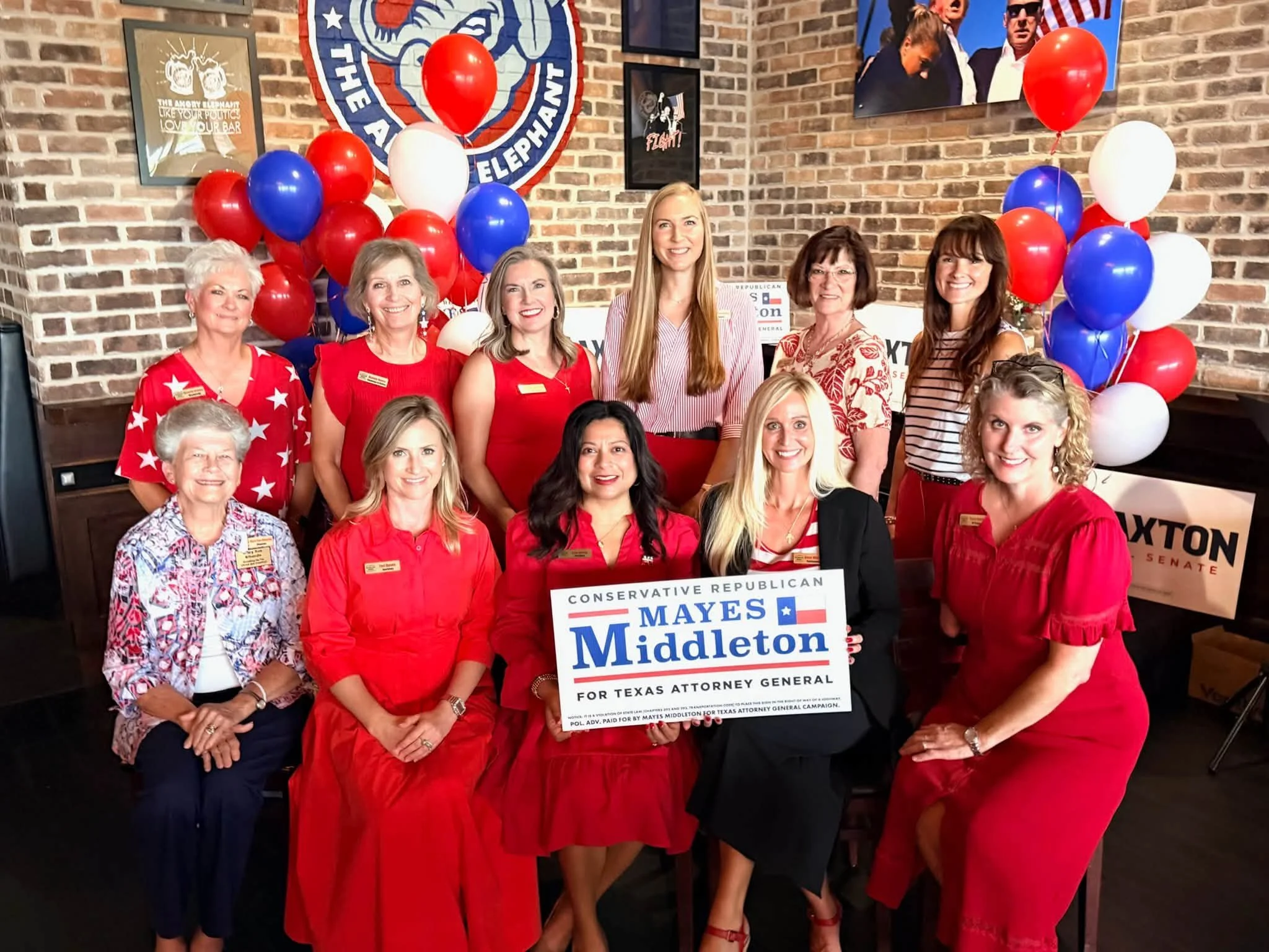 A group of women at a political event for Texas Attorney General candidate Mays Middleton, with balloons and campaign posters in the background.