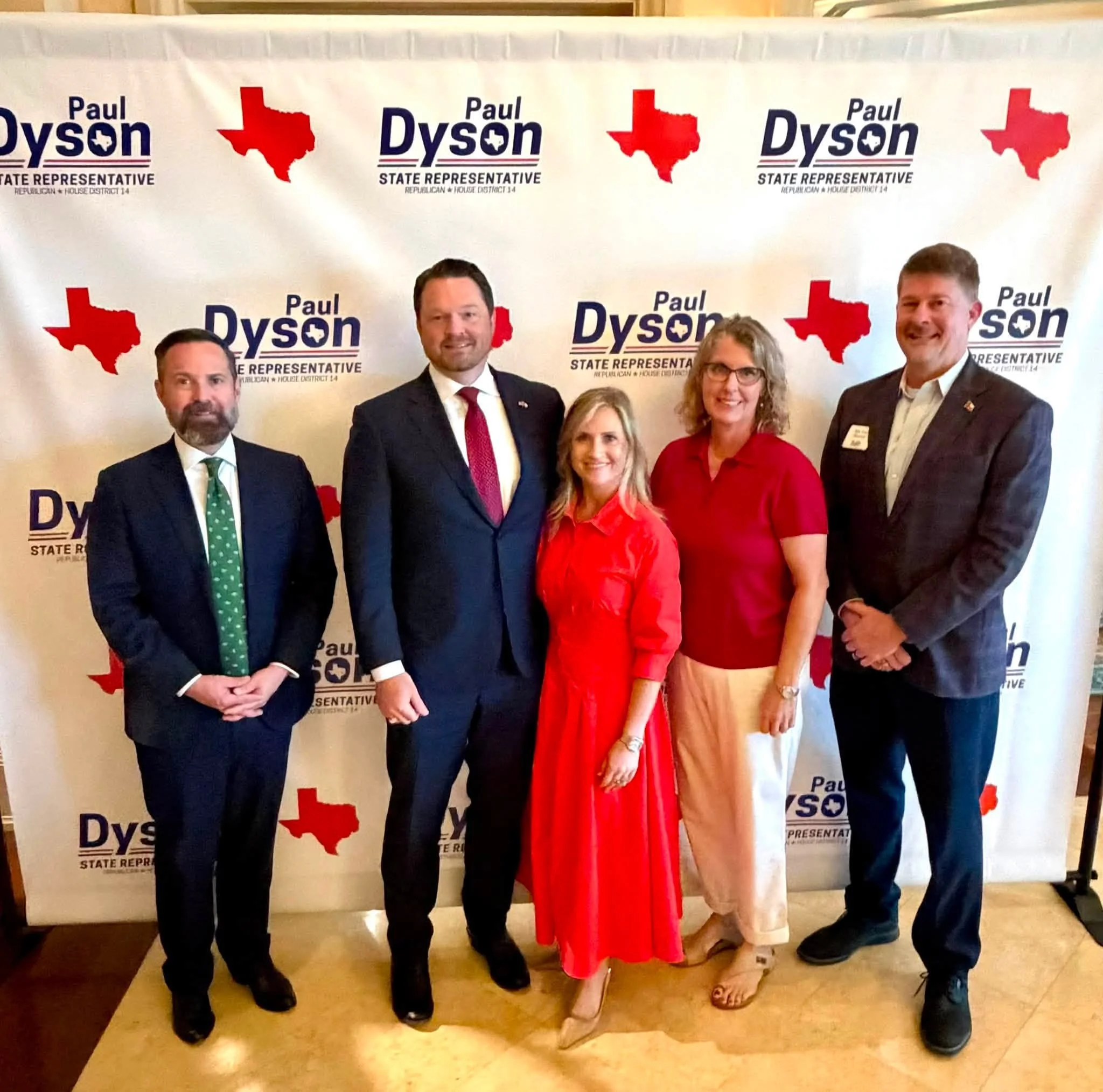 Group of five people standing in front of a political campaign backdrop with the text 'Paul Dyson State Representative' and a red outline of the state of Texas. They are dressed in business attire and smiling.