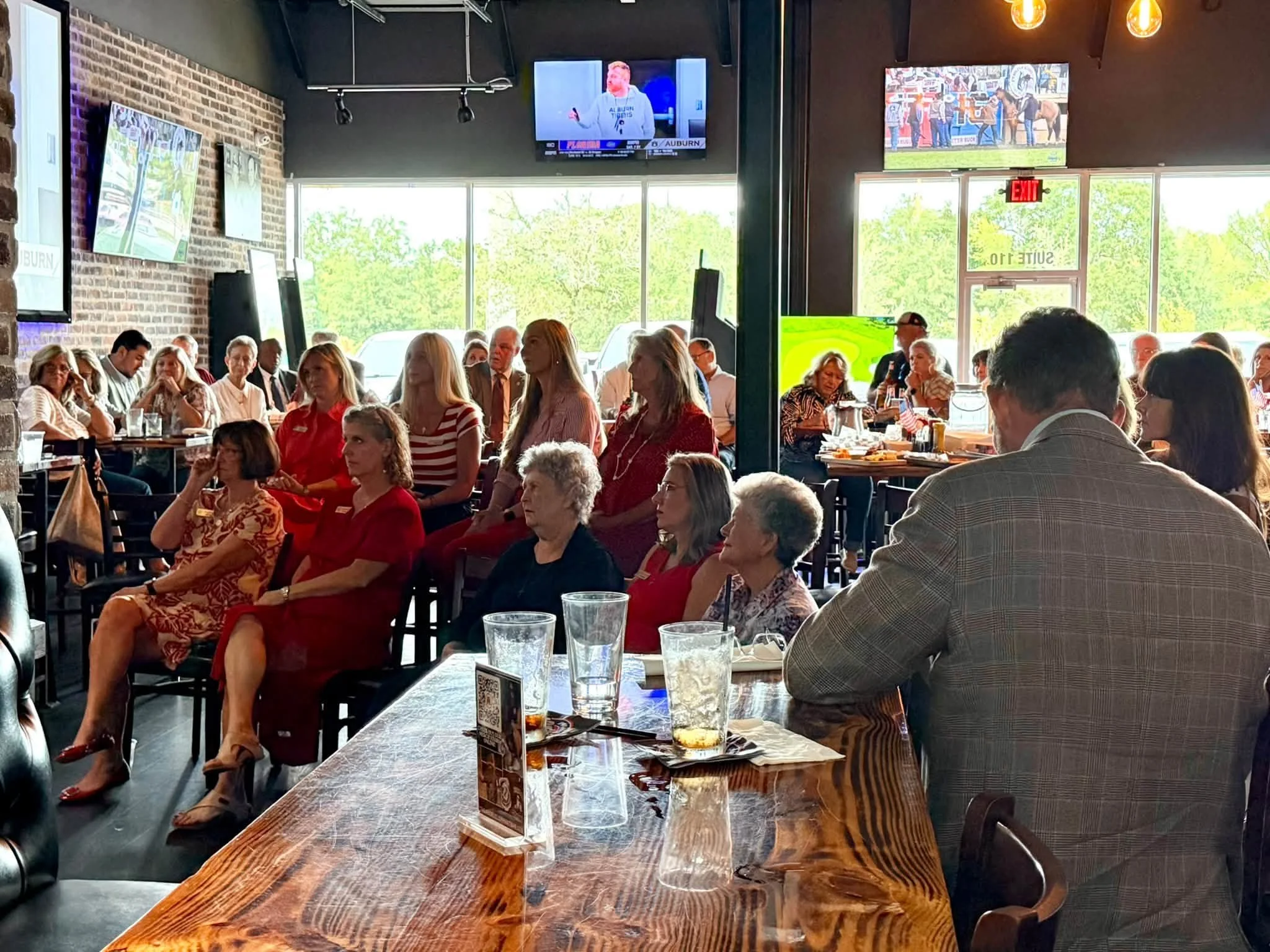 A large group of people sitting and standing inside a restaurant or pub, watching a sports game on multiple televisions mounted on the walls.