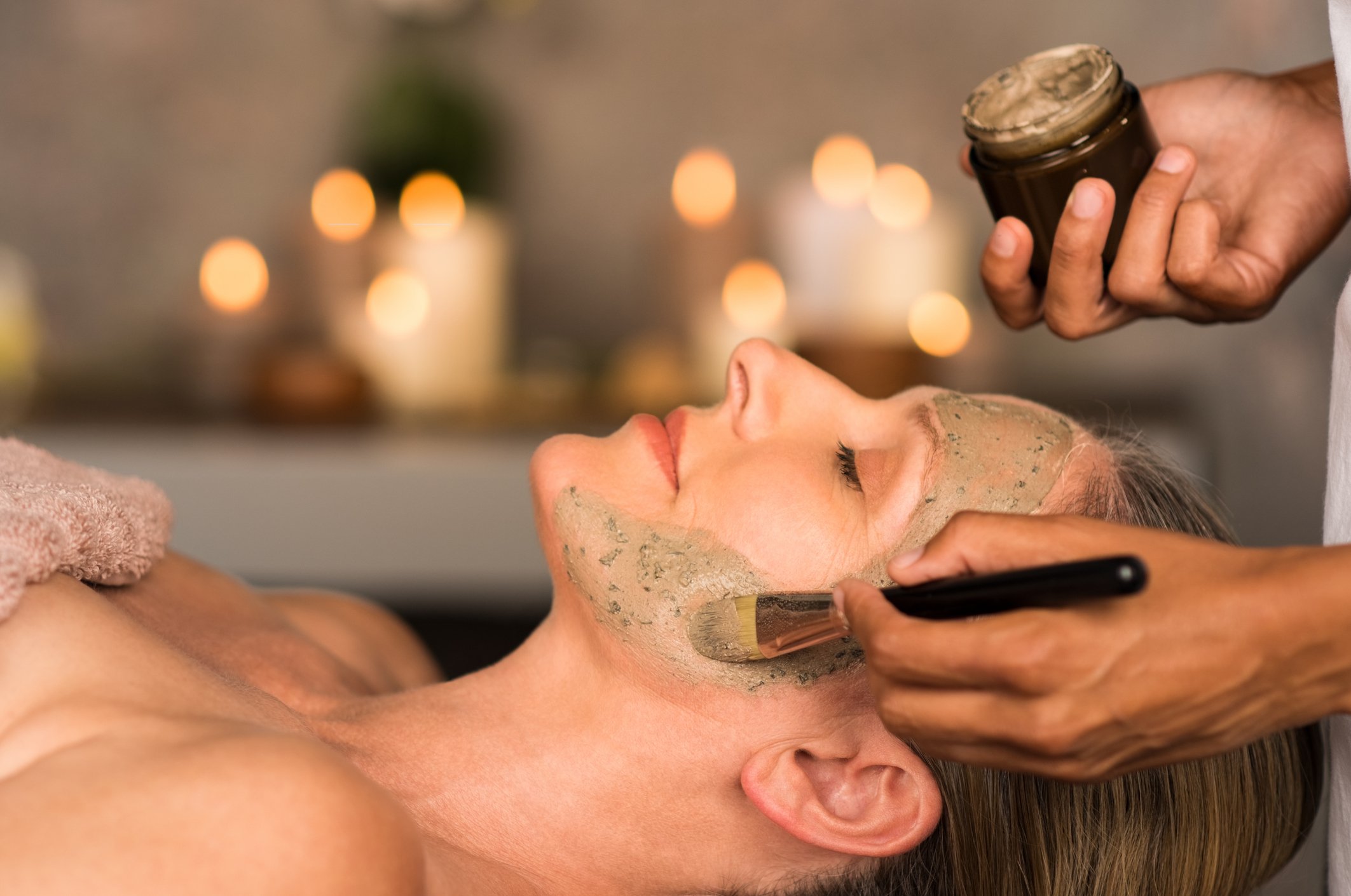 A person lying down with a facial mask, receiving a facial treatment at a spa or skincare clinic, with a professional applying a skincare product on their face.