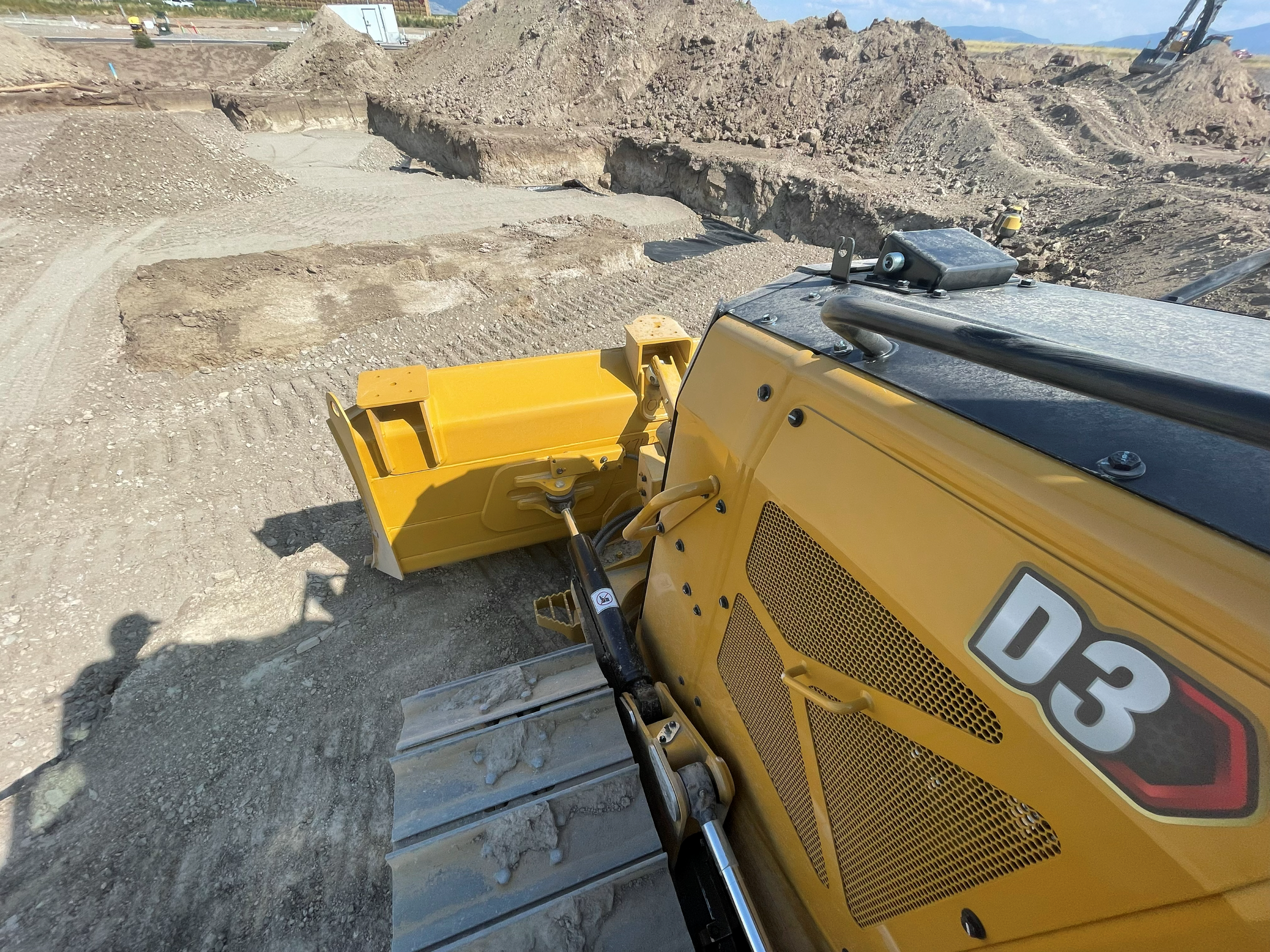 A yellow construction vehicle moving dirt and rocks at a construction site with mounds of earth in the background.
