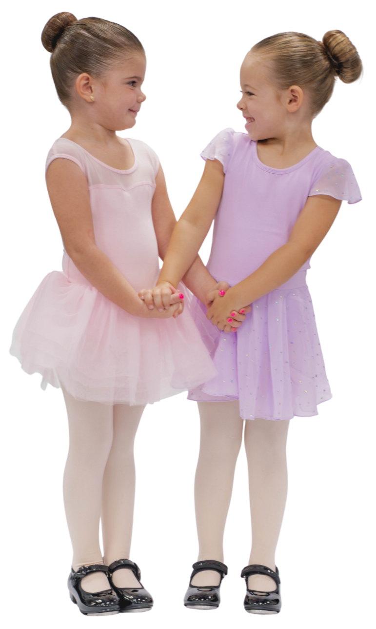 Two young girls in ballet dresses holding hands and smiling at each other
