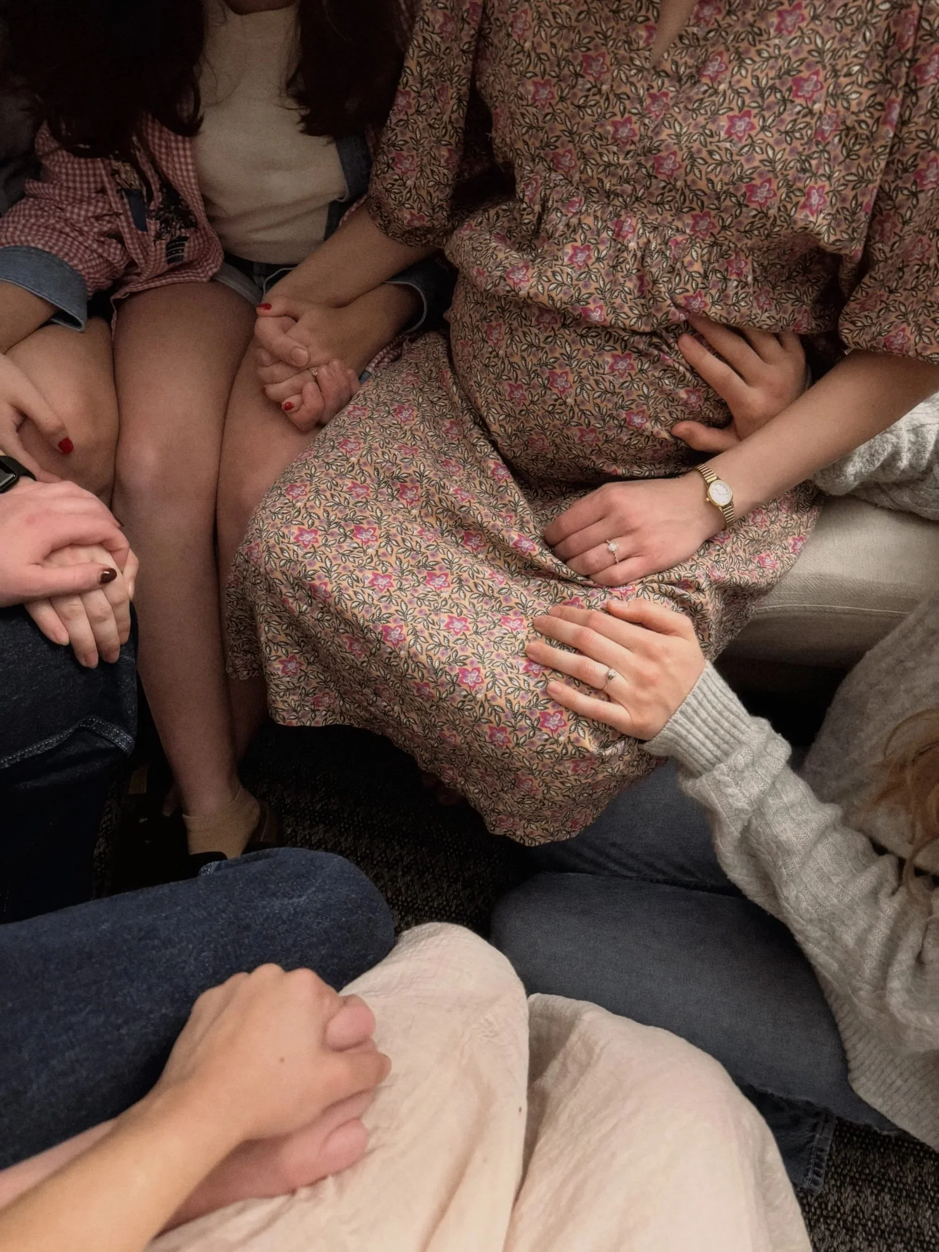 Multiple people sitting close together, holding hands, and wearing casual clothing such as floral, beige, denim, and knit sweaters.