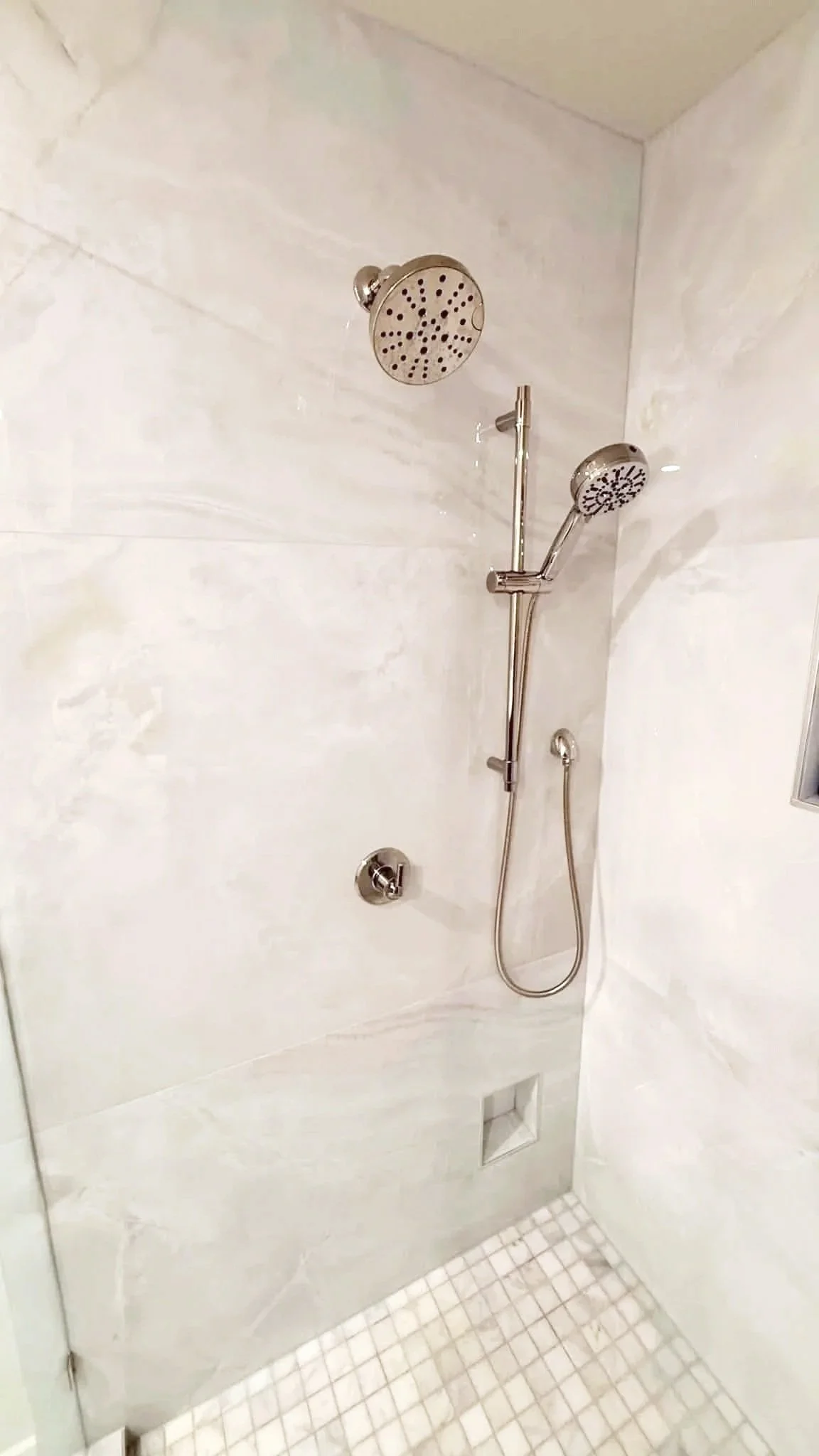 Walk-in shower remodel with light tile walls, built-in niche, and polished nickel shower fixtures.