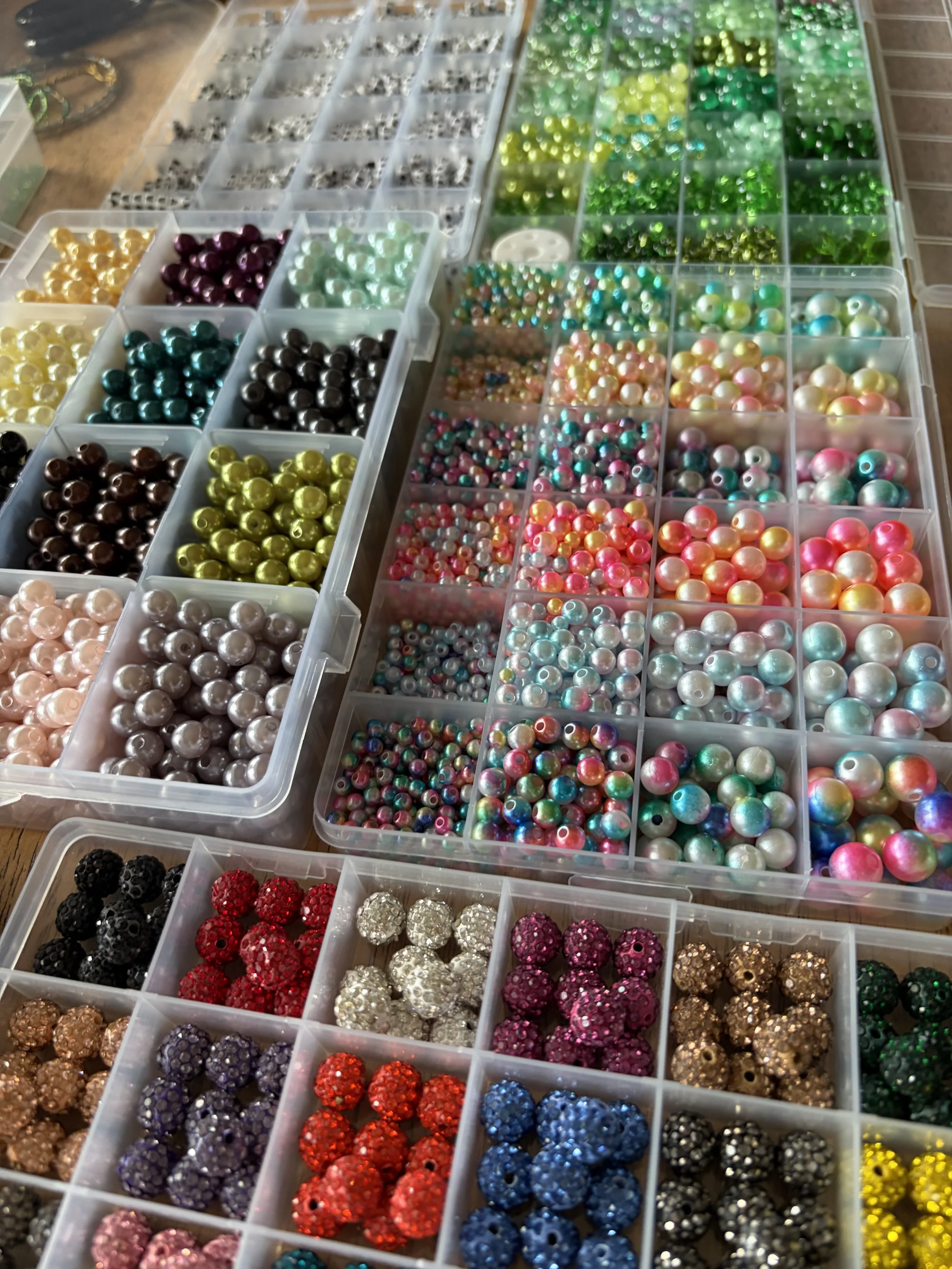 Various containers filled with colorful, shiny beads and rhinestones arranged in rows.