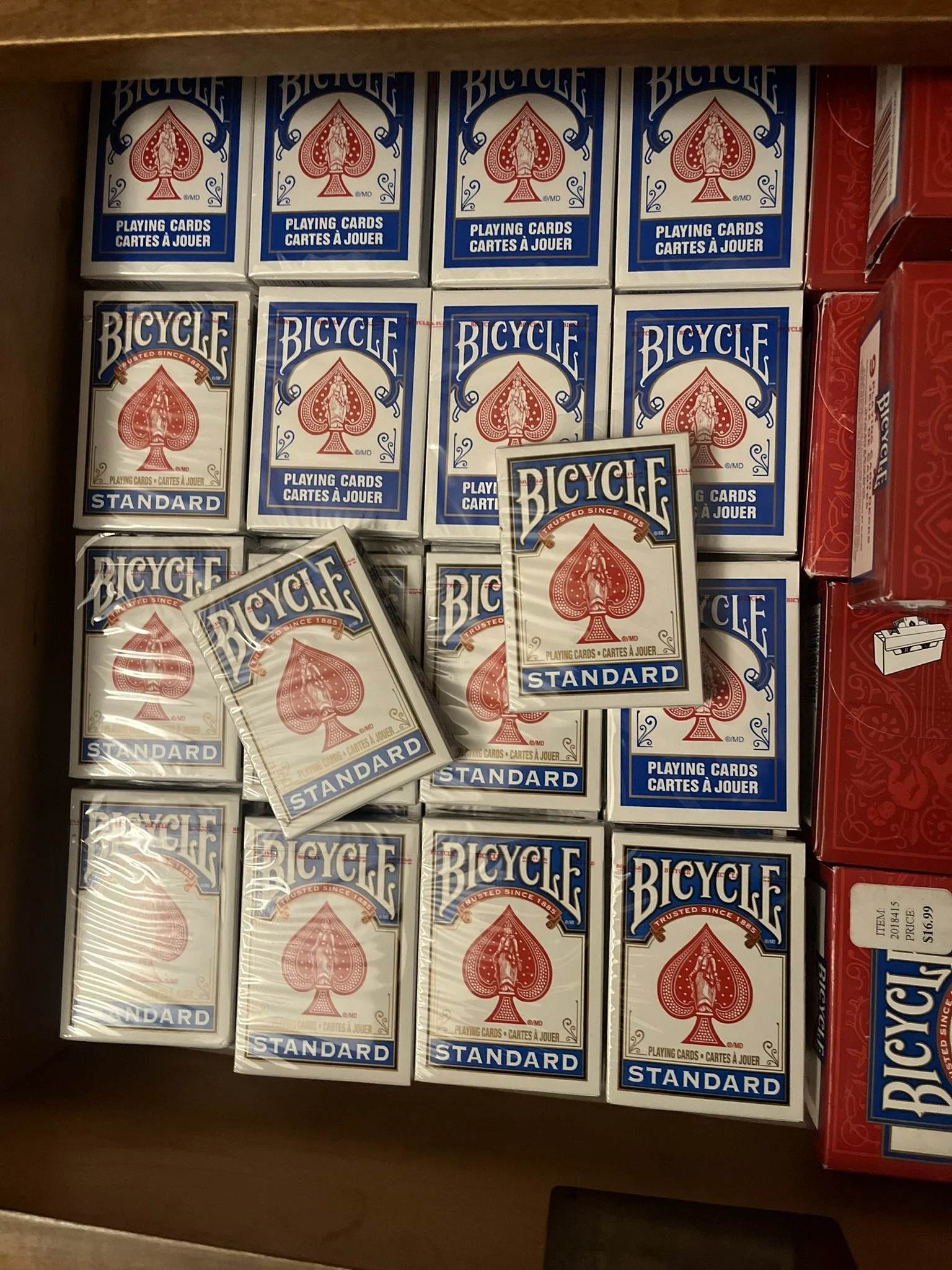 Multiple boxes of Bicycle brand playing cards in a store shelf. The boxes are mainly white with blue and red accents, with some boxes showing the word 'STANDARD' and others the word 'TRUSTED SINCE 1885.'